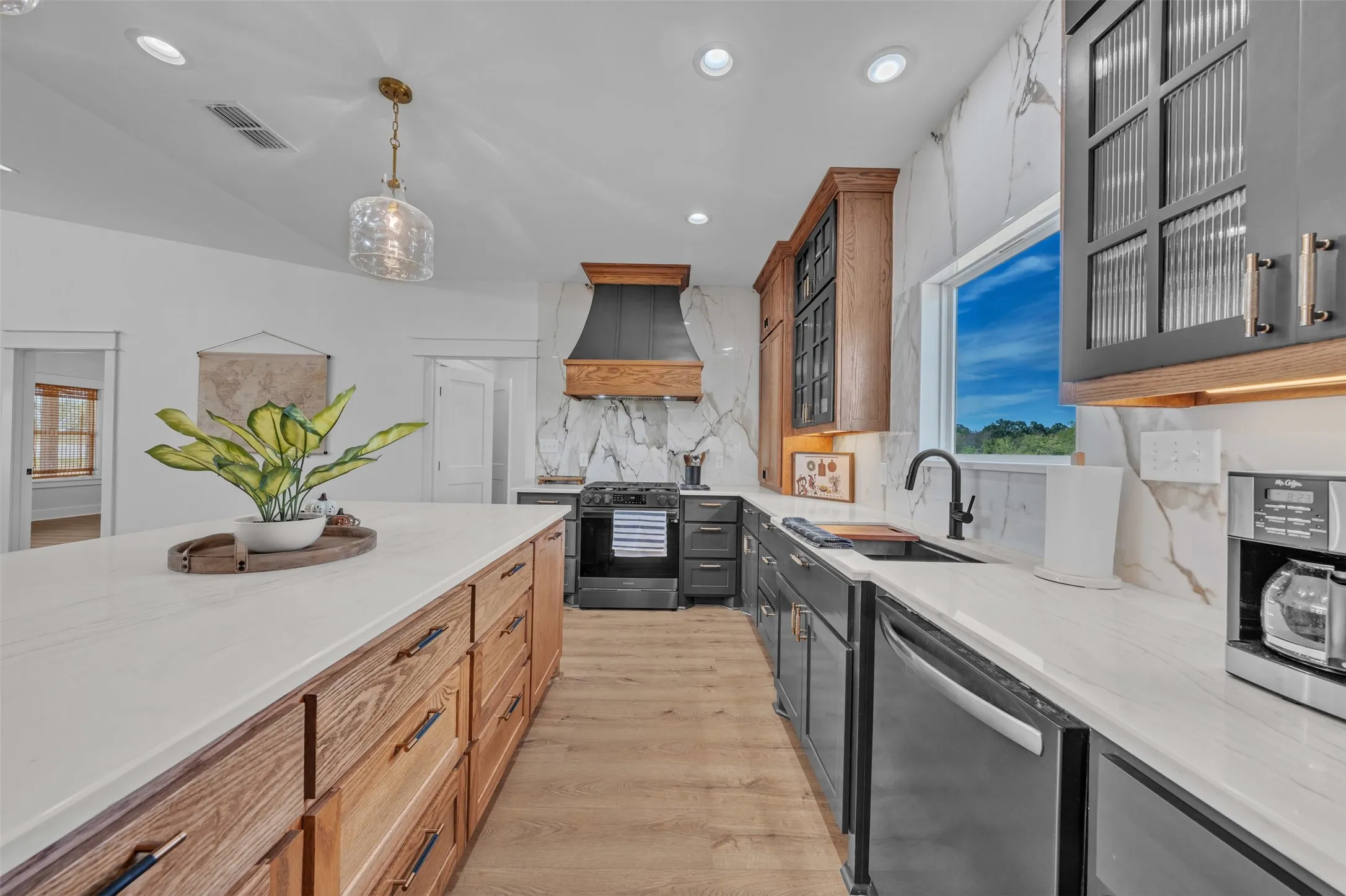 Kitchen featuring an expansive island with a light-toned countertop, wood-finish flooring, and a range hood with wood and dark metal accents
