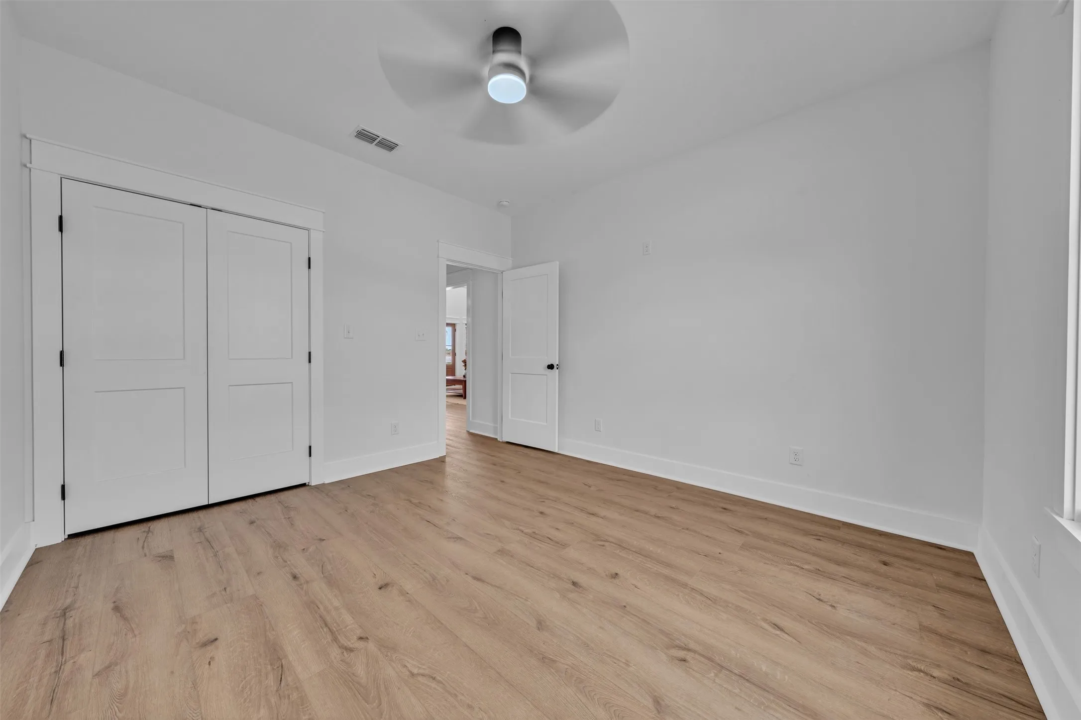 Neutral wall finishes, wood-finish flooring, ceiling fan with integrated lighting, and white paneled doors