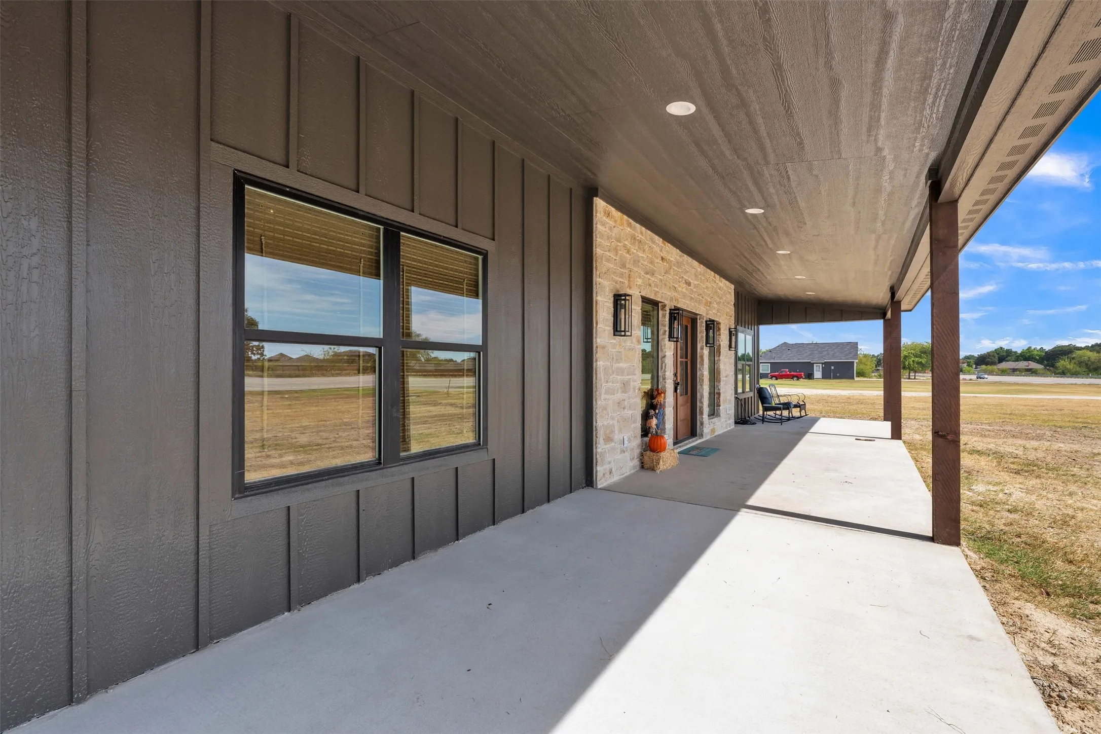 Board-and-batten siding, stone facade, covered concrete patio, recessed lighting, and dark-framed windows
