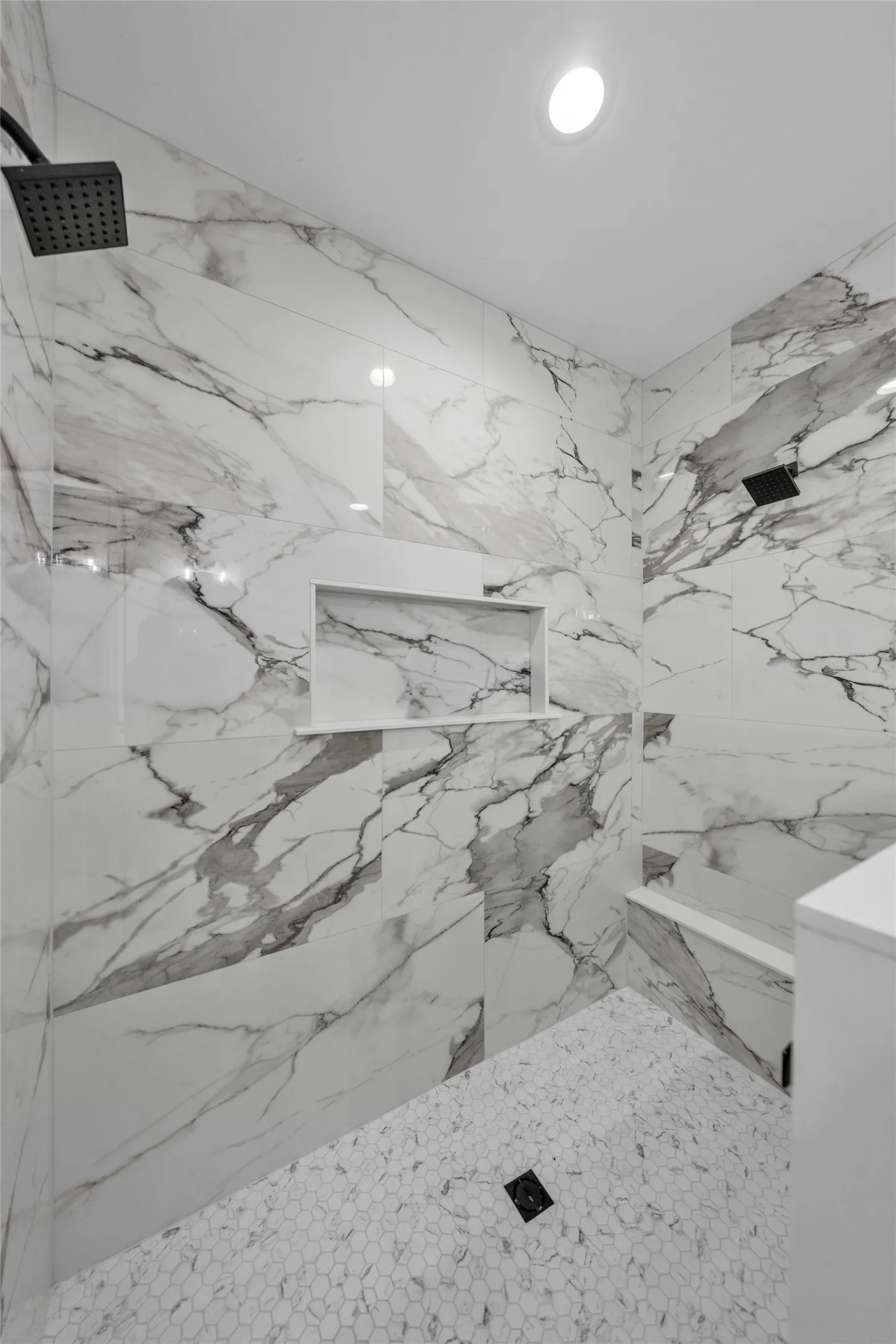 Walk-in shower with full-height patterned wall tiling, built-in recessed shelf, built-in bench, and hexagon mosaic floor tiling