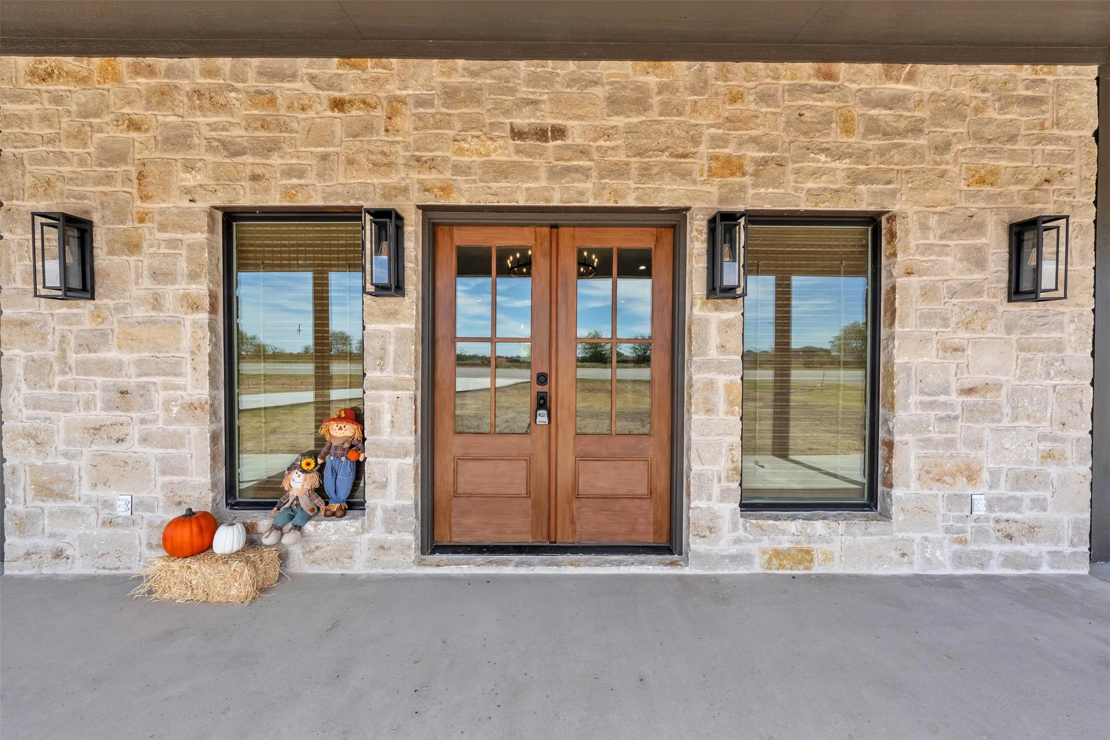 Stone facade with a double-door entry featuring glass panels, flanked by two large windows, and illuminated by exterior sconces