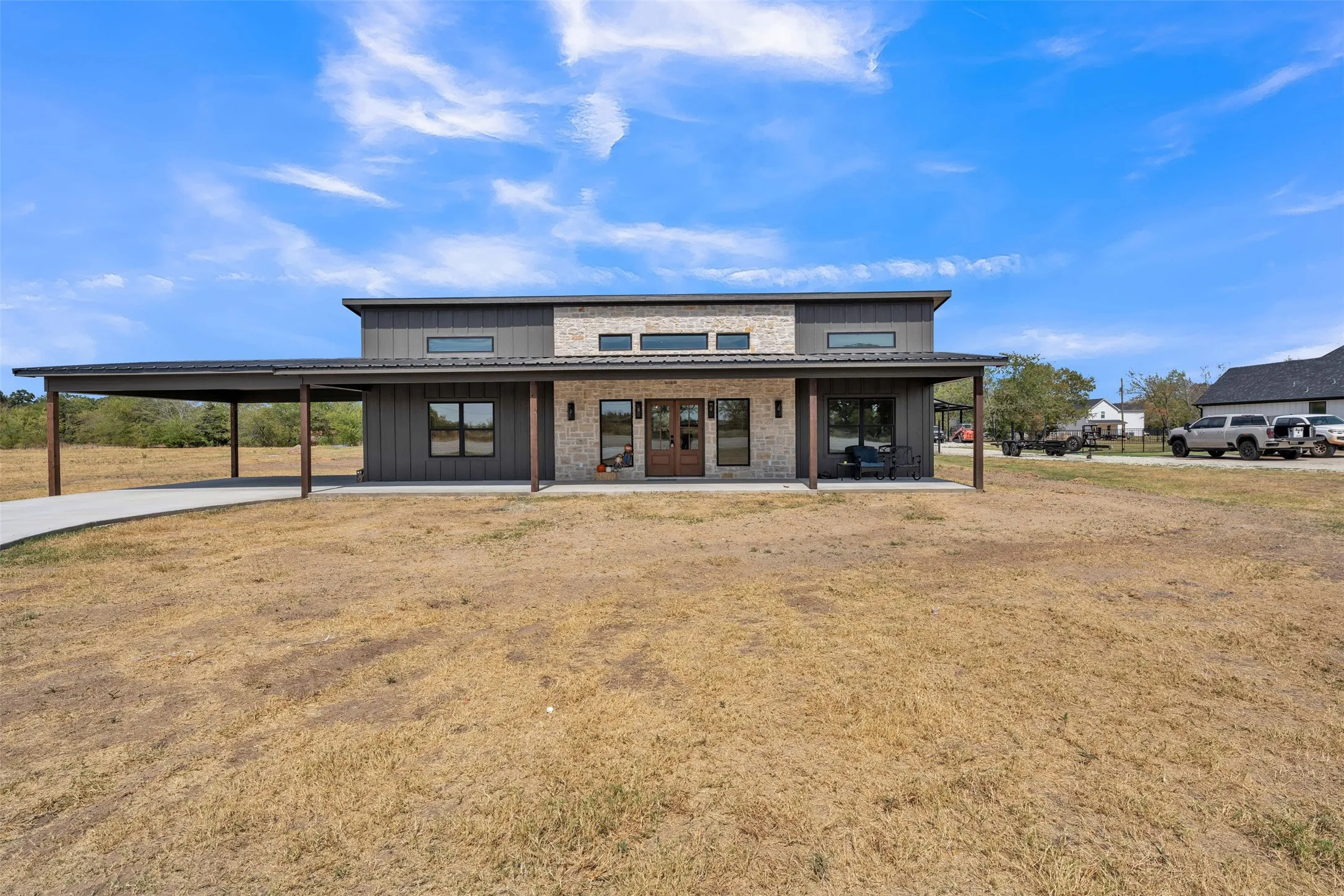 Modern exterior featuring a stone accent wall, board and batten siding, dark-framed windows, and an expansive covered carport