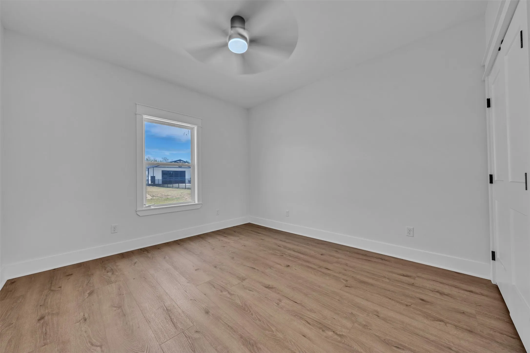 Wood-finish flooring, white trim, and a ceiling fan with integrated lighting