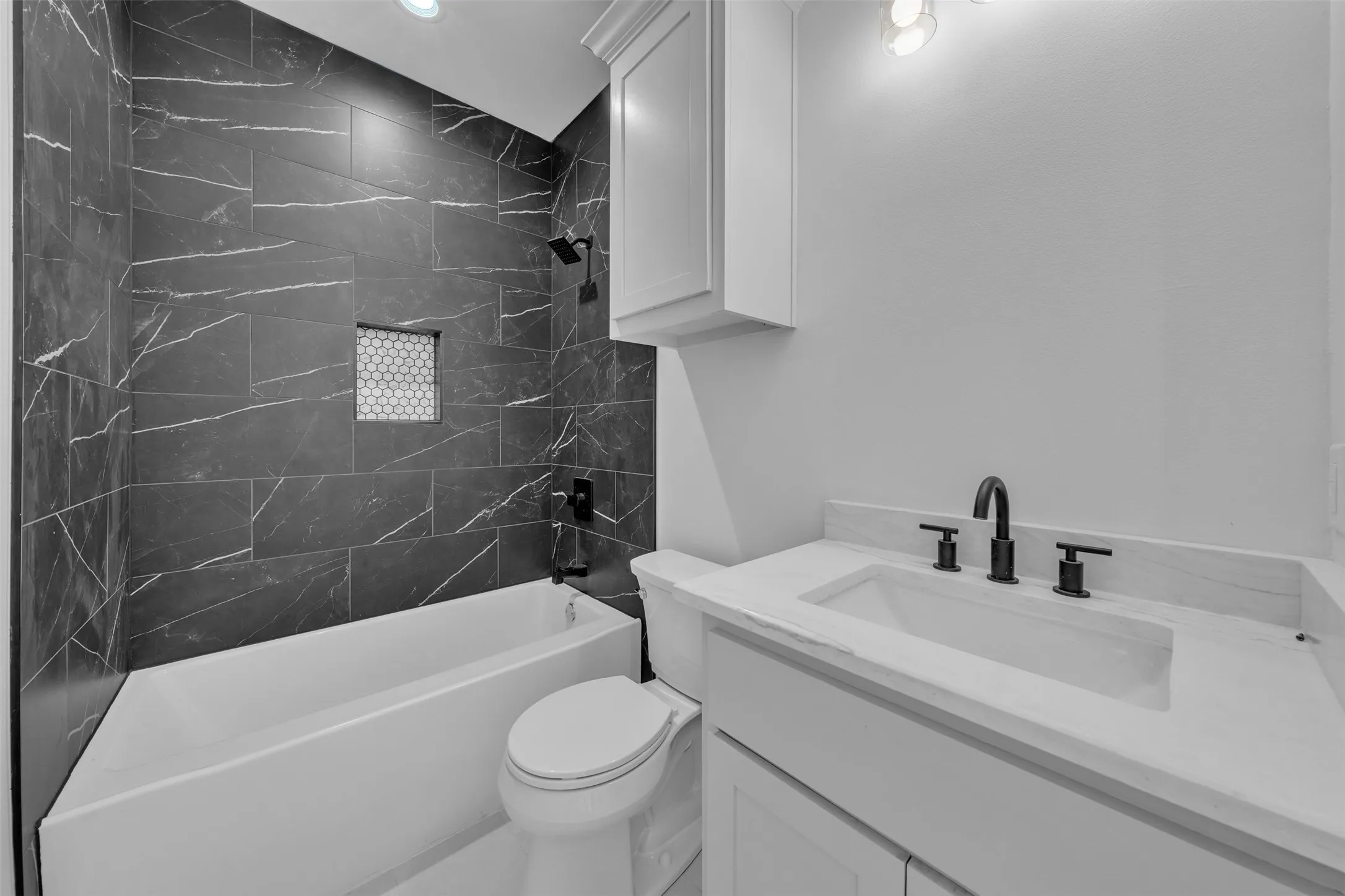Bathtub with dark-toned tile surround, recessed shelf with mosaic tile, and matte black fixtures