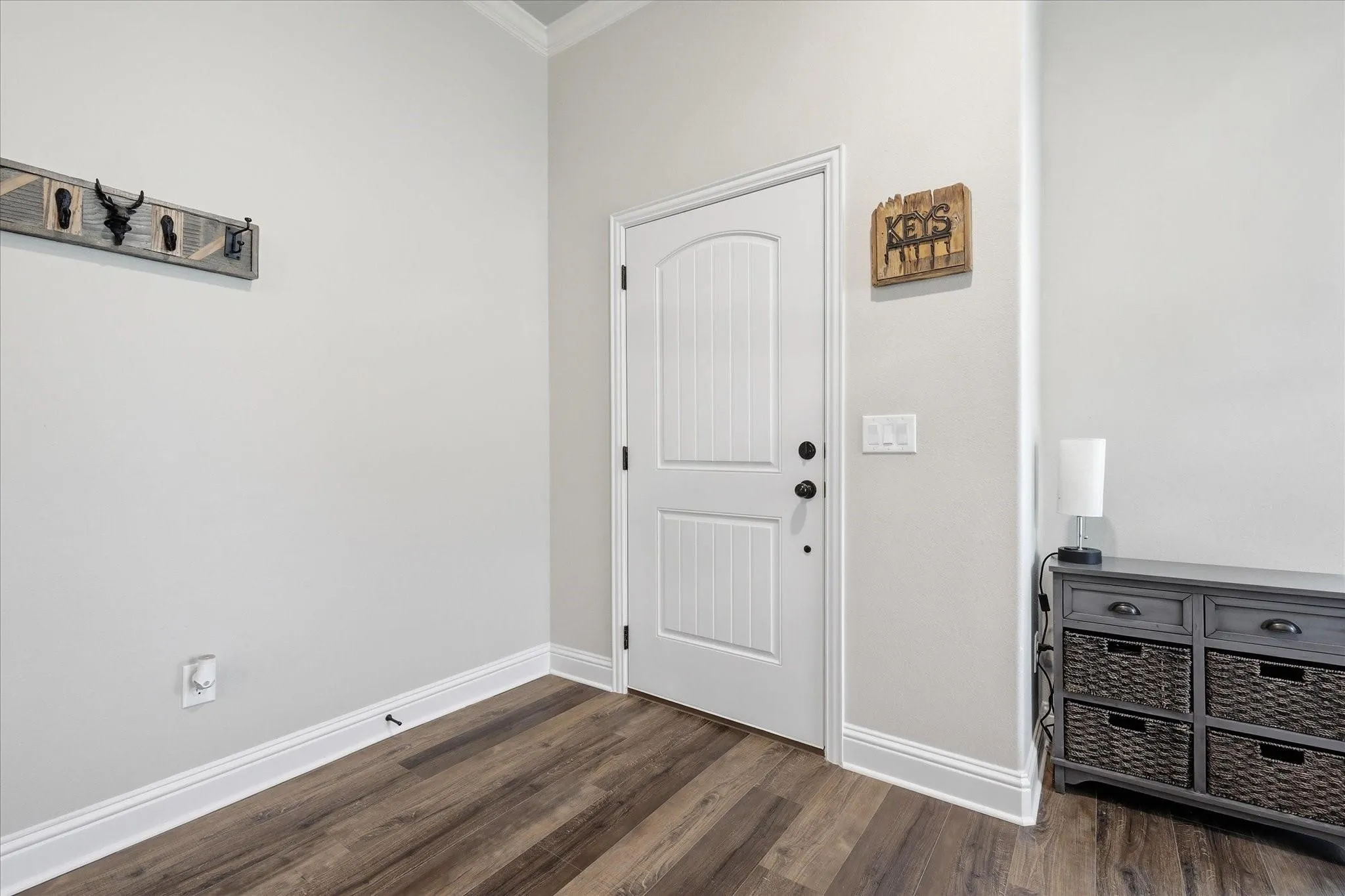 Wood-finish flooring with white trim, a white paneled door with black hardware, and light-colored walls