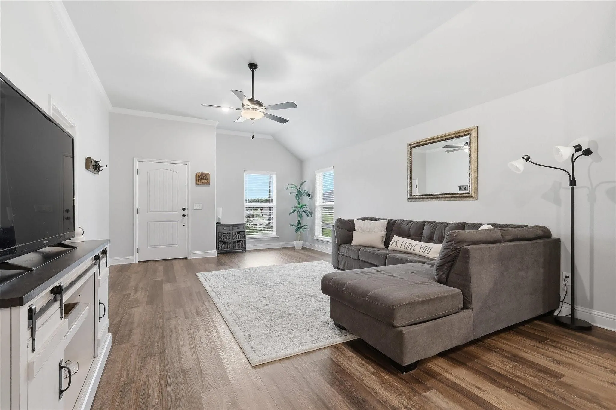 Vaulted ceiling, wood-finish flooring, white trim, ceiling fan with lighting, multiple windows