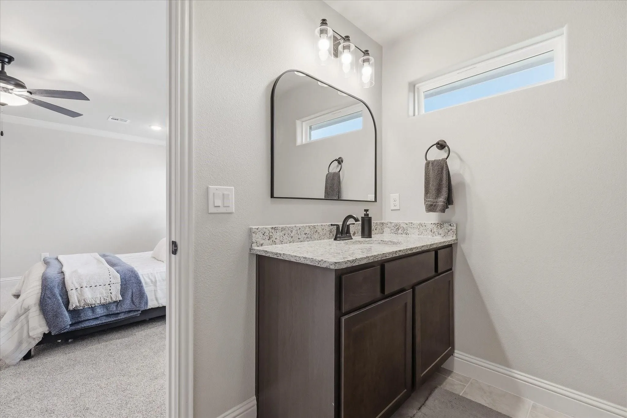 Bathroom vanity featuring a quartz countertop, dark wood-finish cabinetry, and a black framed arch mirror