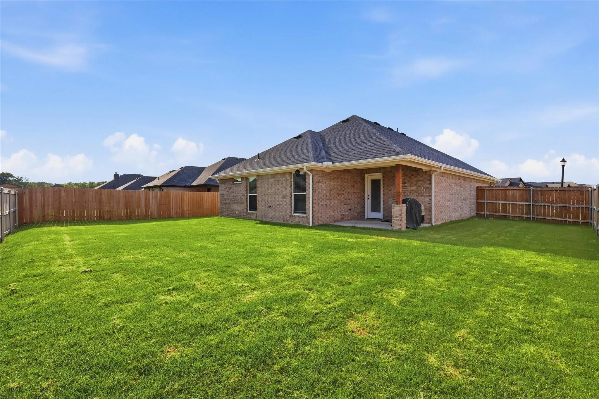 Expansive backyard featuring a manicured lawn, full perimeter privacy fencing, and a covered patio with a wood-clad support pillar
