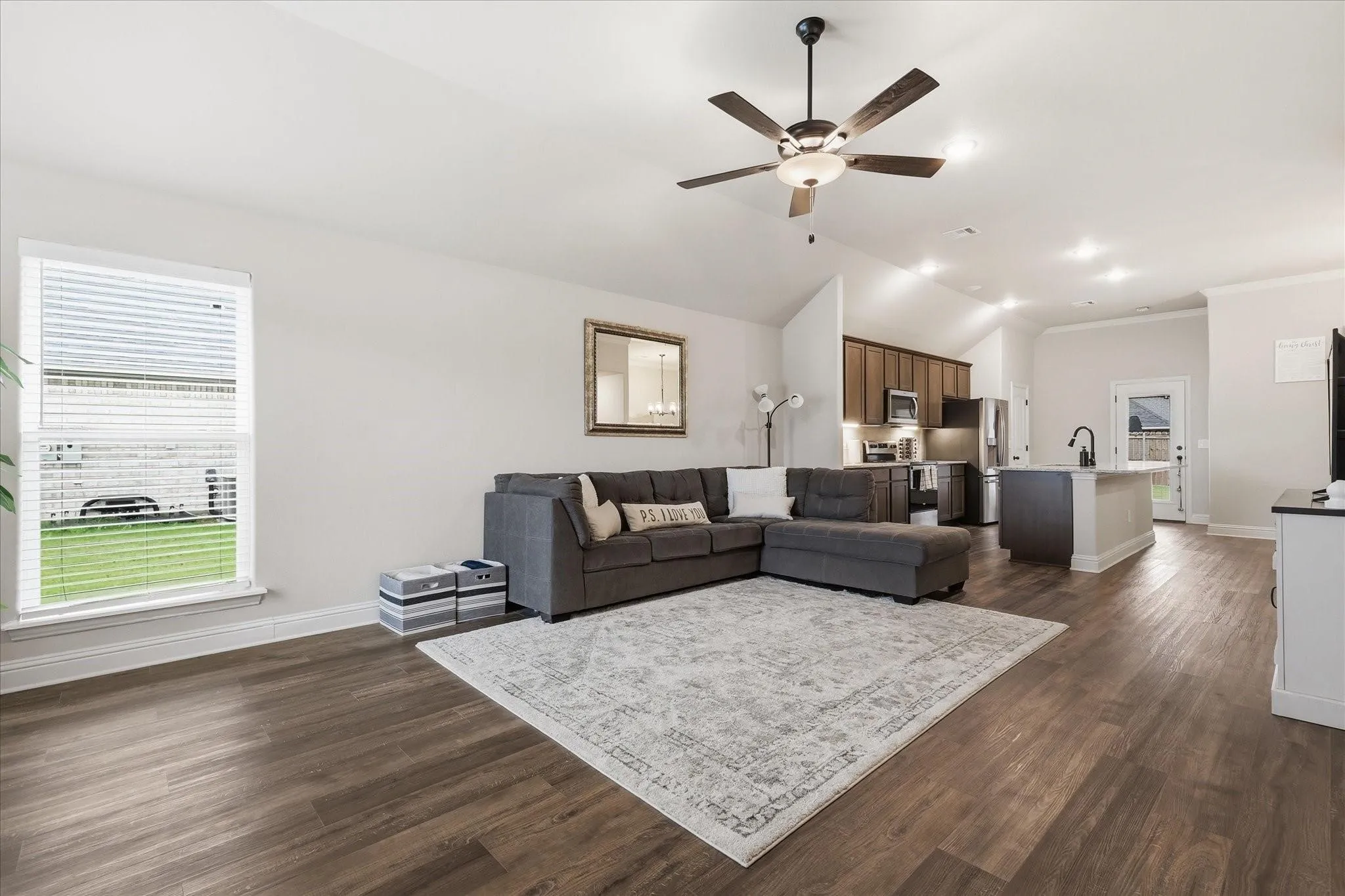 Open-concept living area with wood-finish flooring, vaulted ceilings, and a ceiling fan