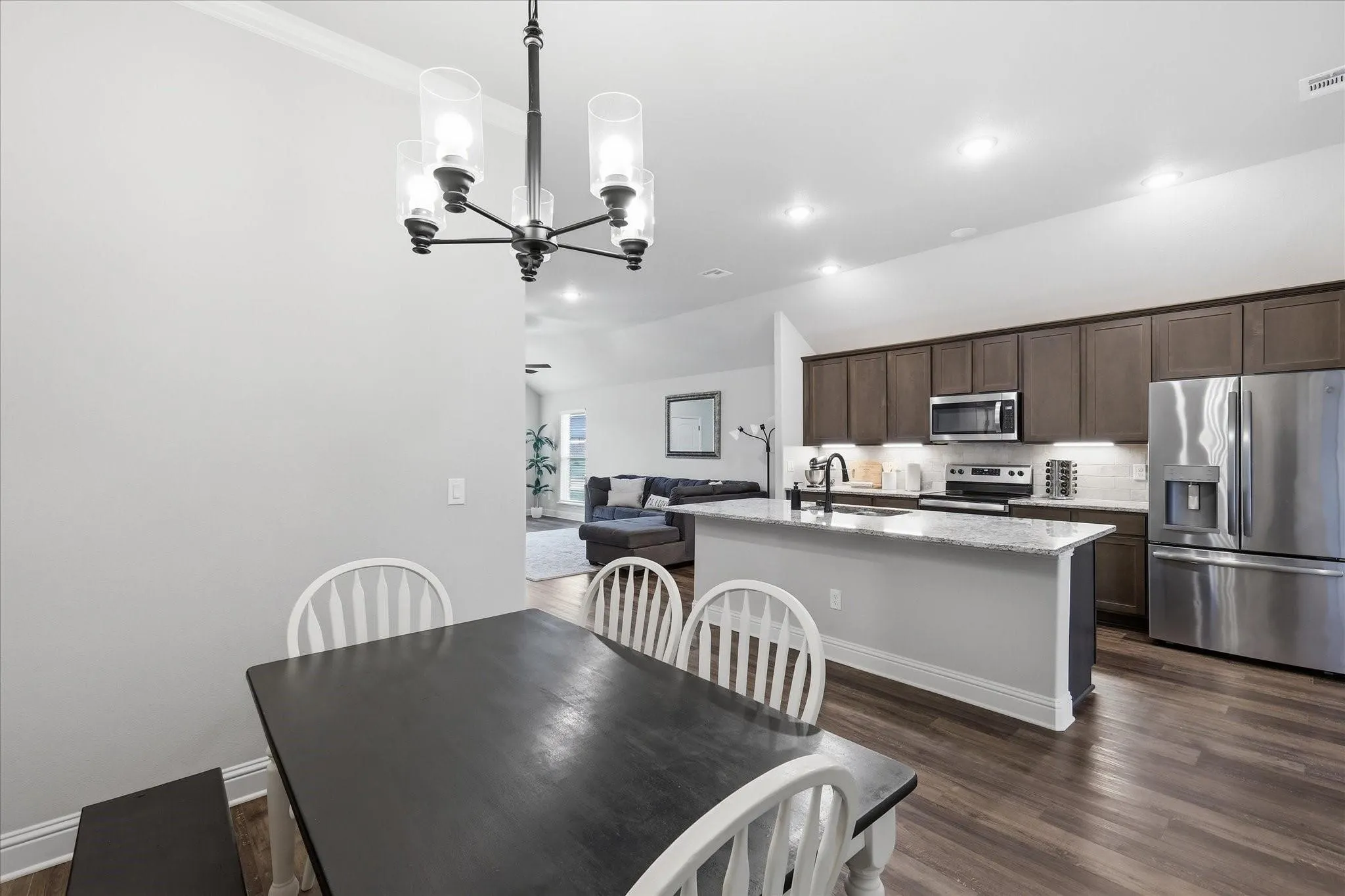 Open-concept living area featuring wood-finish flooring, a kitchen island with stone countertop, stainless steel appliances, recessed lighting, and a modern chandelier
