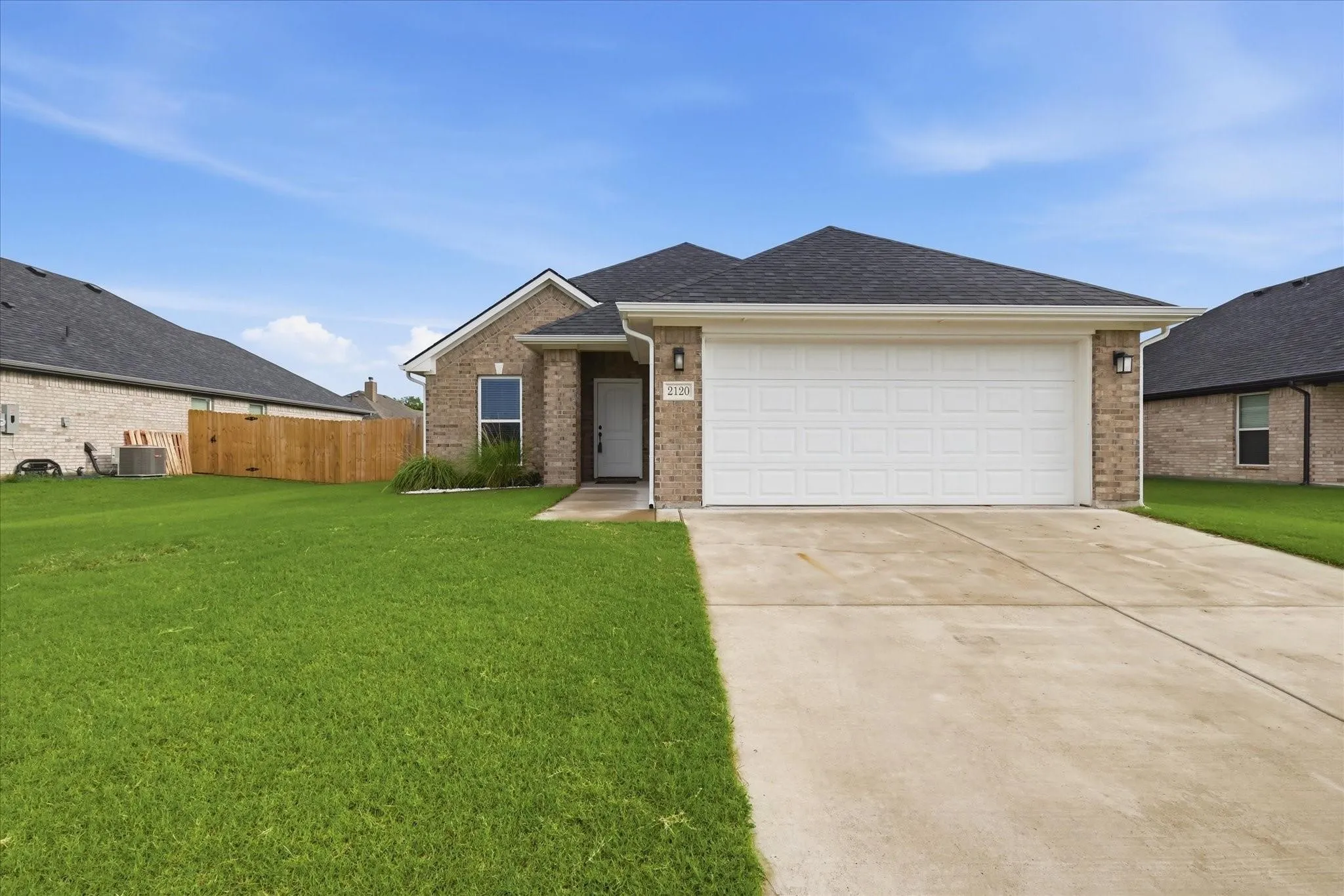 Brick exterior, attached two-car garage, concrete driveway, front entry door, and manicured lawn