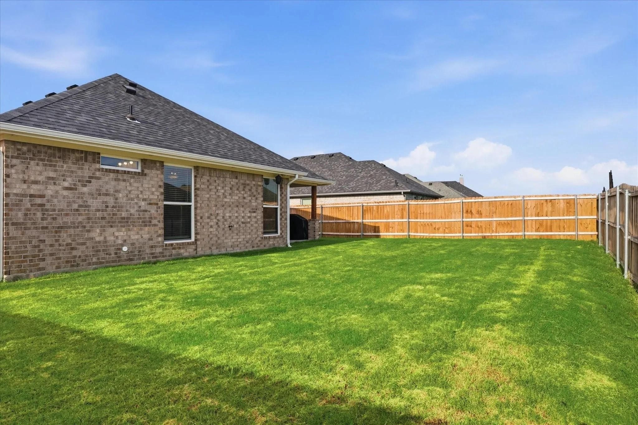 Expansive backyard featuring a manicured lawn, full wood privacy fencing, and a brick exterior