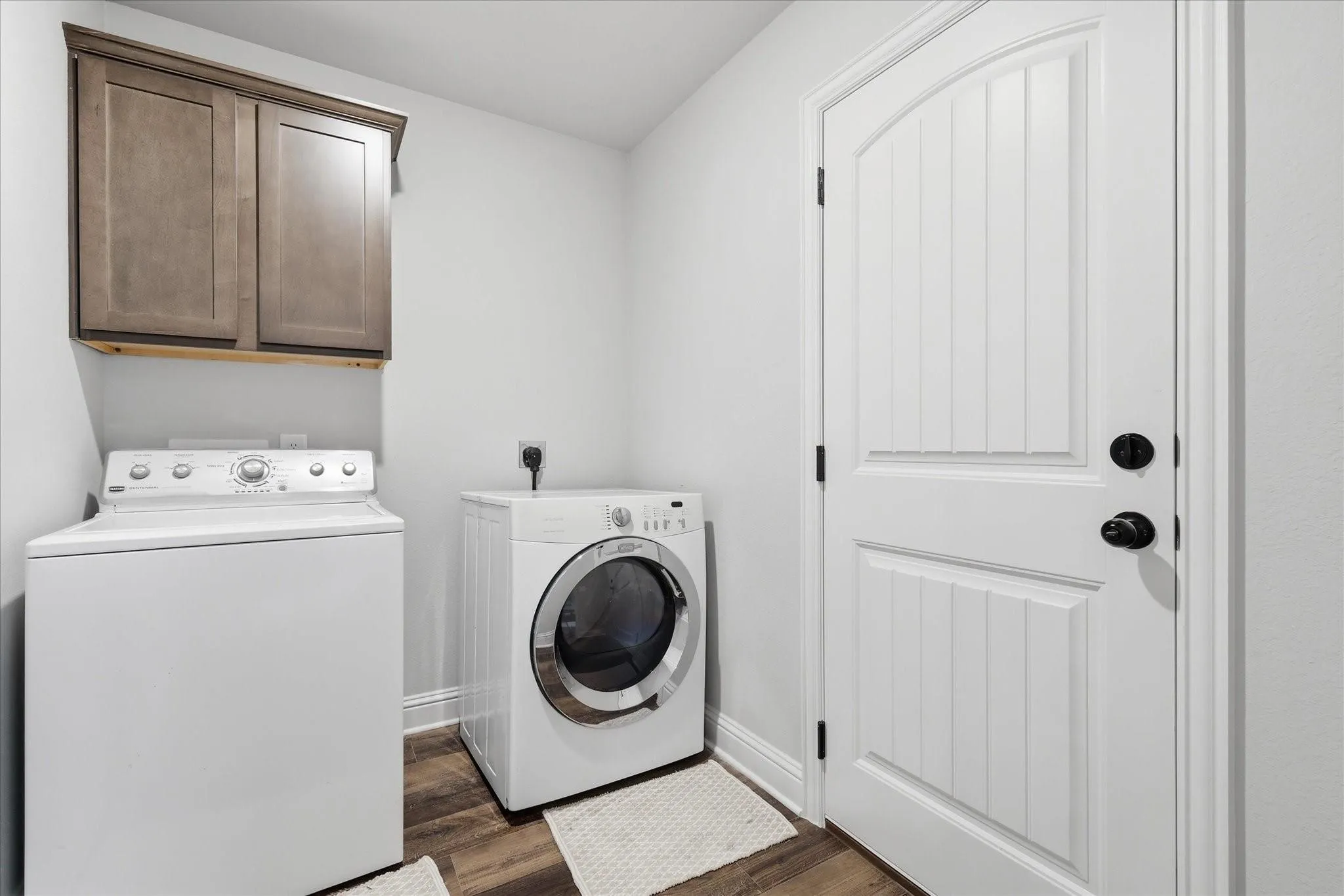 Laundry area featuring wood-finish flooring, built-in cabinetry, and a paneled door with matte black hardware