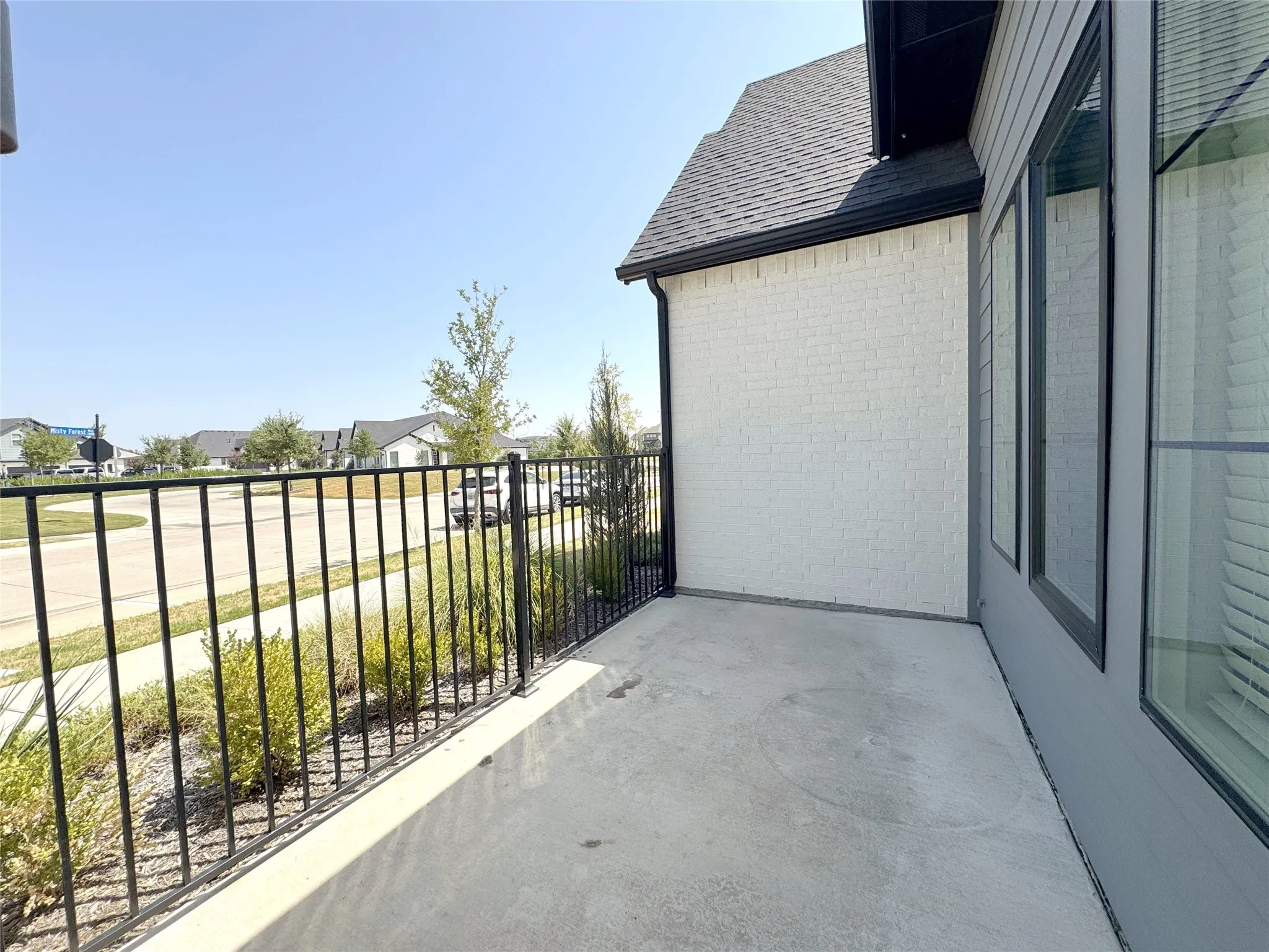 Private concrete patio featuring a black metal railing and landscaping