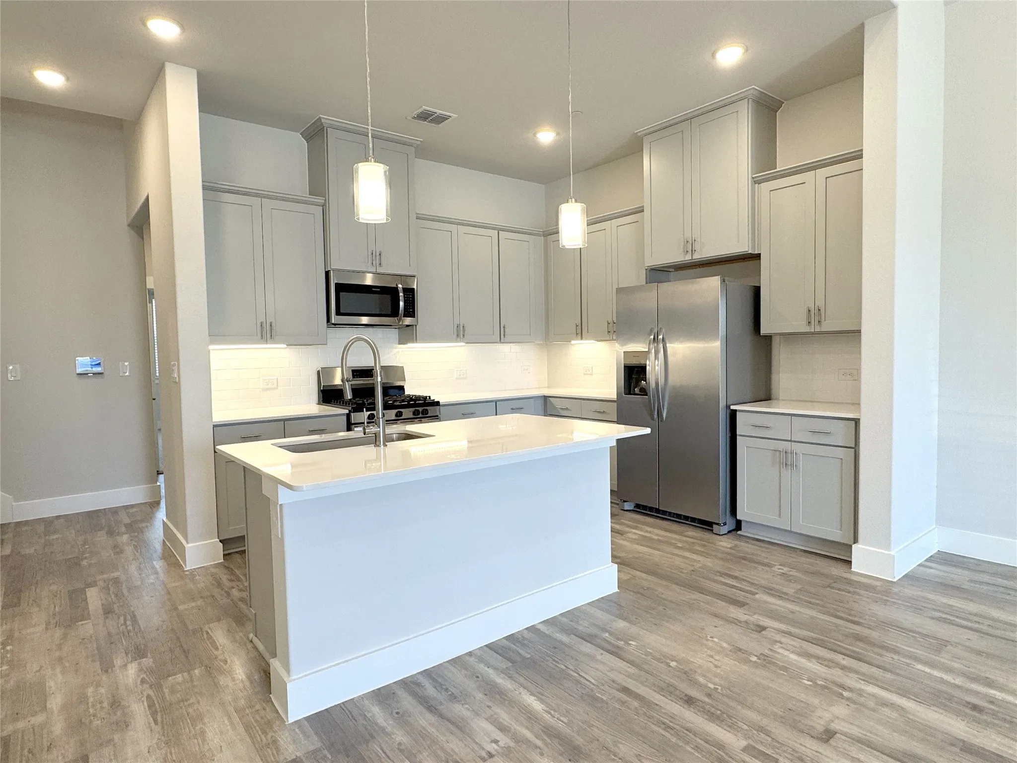 Modern kitchen featuring light gray cabinetry, stainless steel appliances, a white subway tile backsplash, and light wood-finish flooring