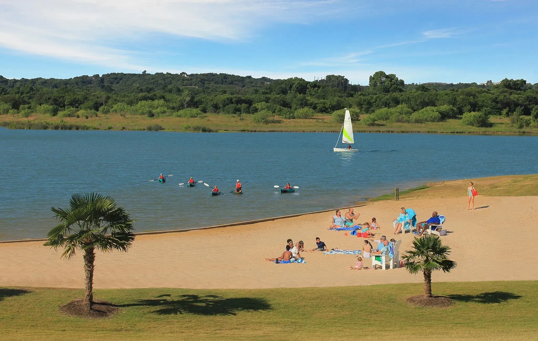 Expansive waterfront property featuring a sandy beach, mature palm trees, clear blue water, and a tree-lined horizon