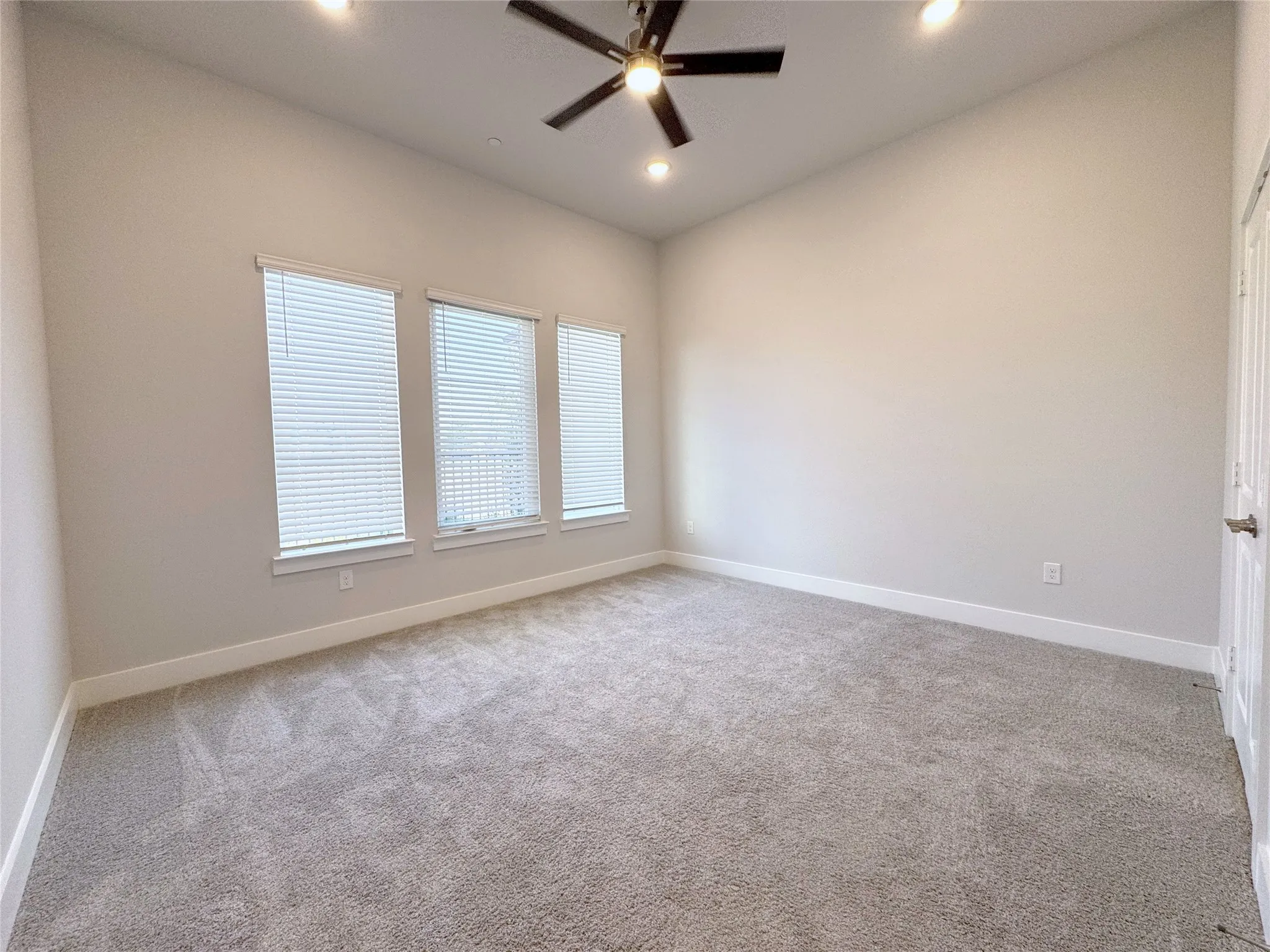 Spacious room featuring three windows with blinds, plush gray carpeting, high ceilings, and recessed lighting