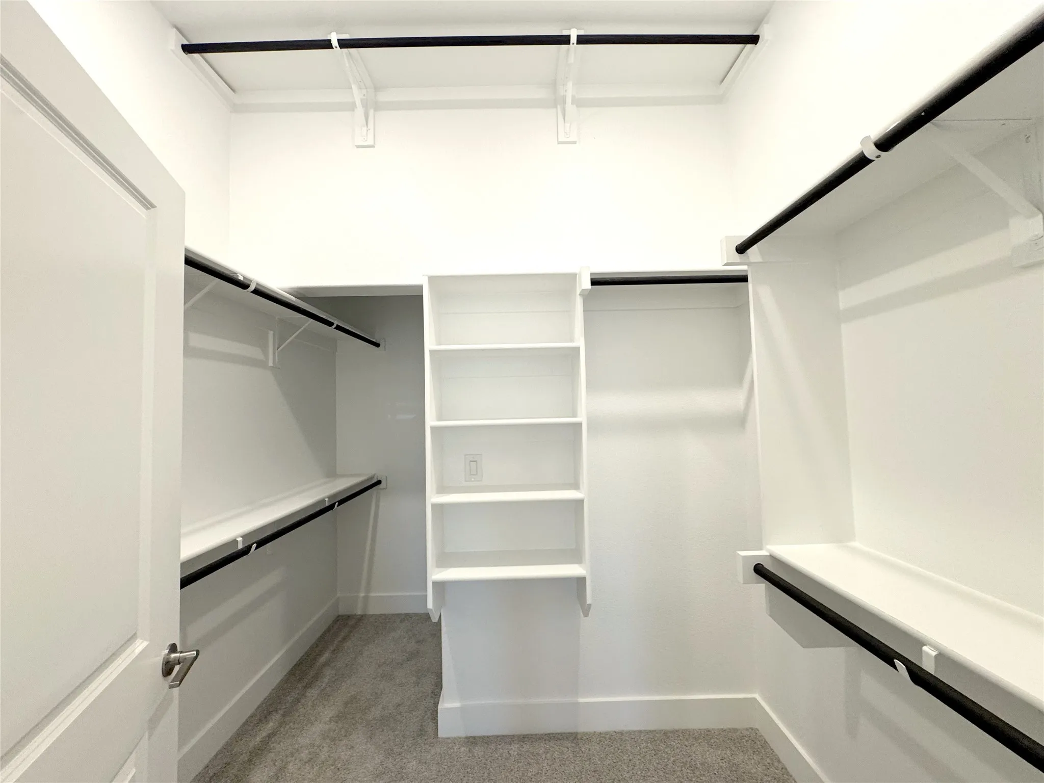 Walk-in closet featuring built-in shelving, multiple hanging rods, and light gray carpeting