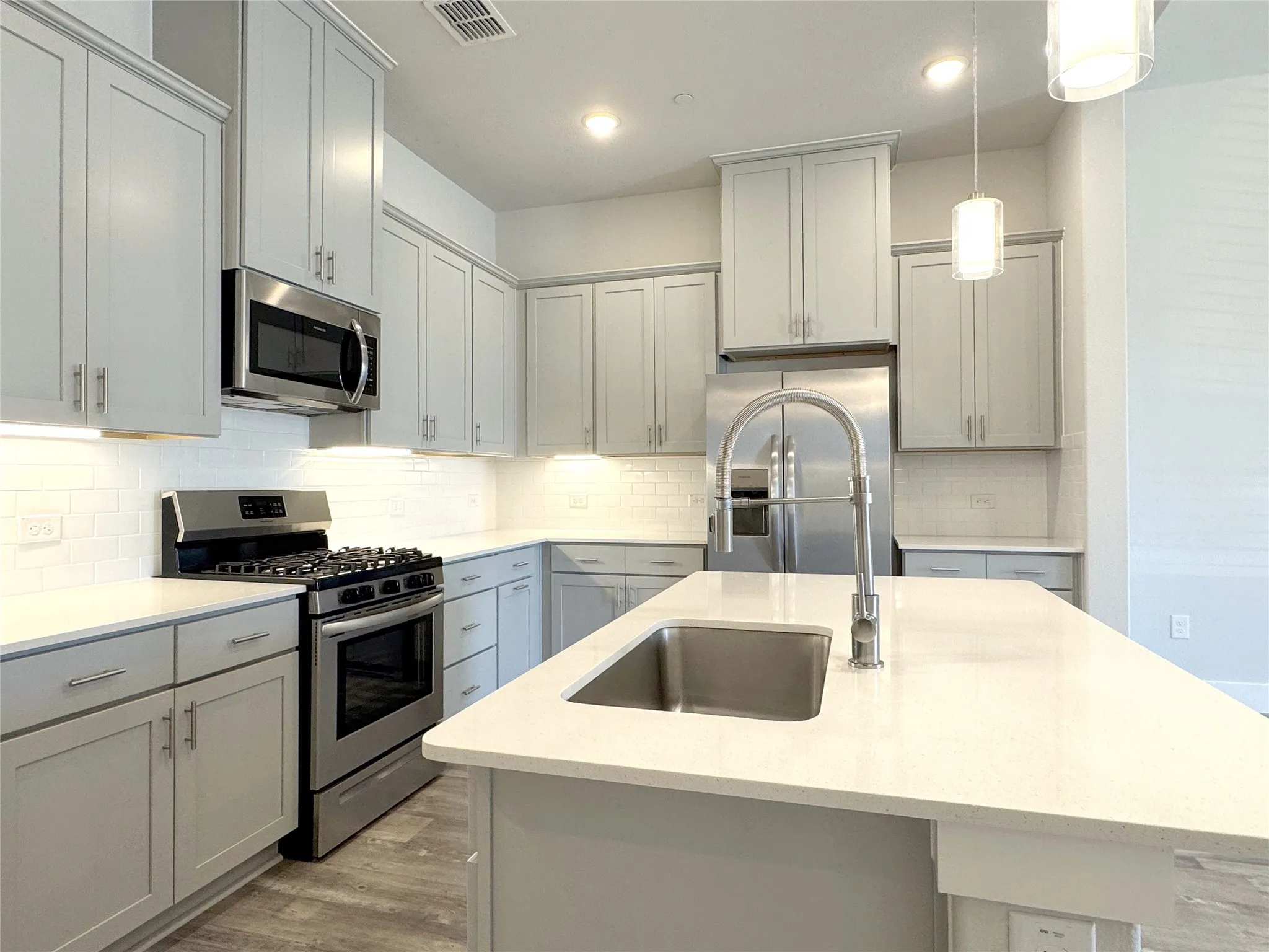 Contemporary kitchen featuring light gray cabinetry, stainless steel appliances, white subway tile backsplash, light-colored countertops, and wood-finish flooring