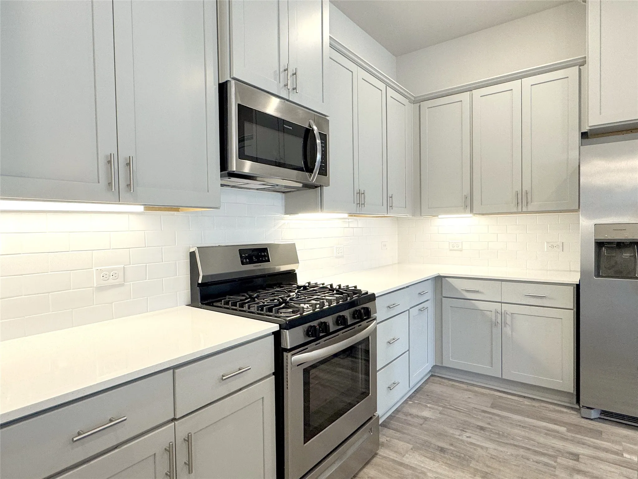 Contemporary kitchen featuring light gray cabinetry, stainless steel appliances, white subway tile backsplash, and light-toned countertops