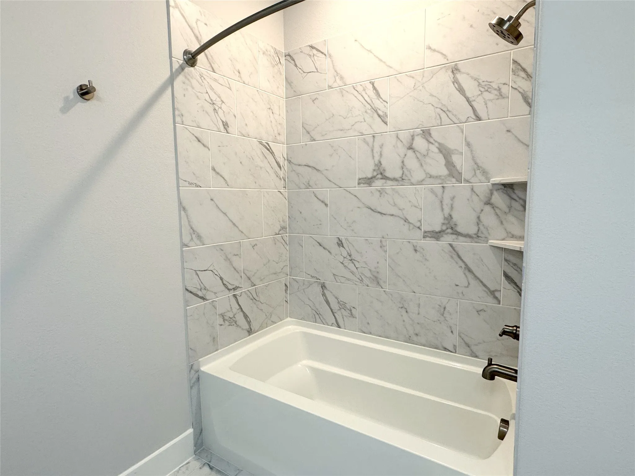 Bathtub shower combination featuring white subway tile with gray veining, recessed shelving, and oil-rubbed bronze fixtures