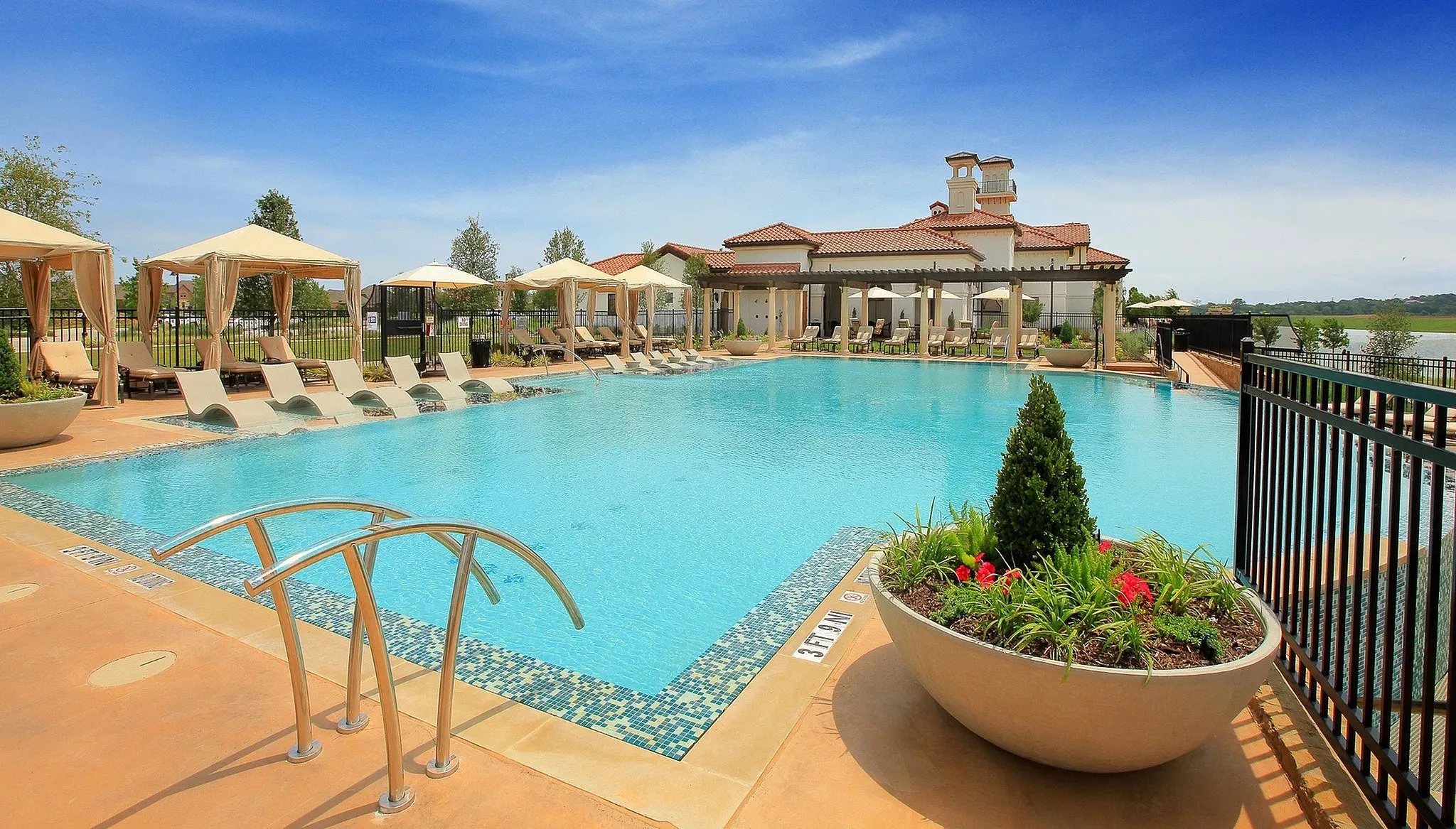 Expansive outdoor swimming pool featuring a mosaic tile border, integrated steps, and sun loungers