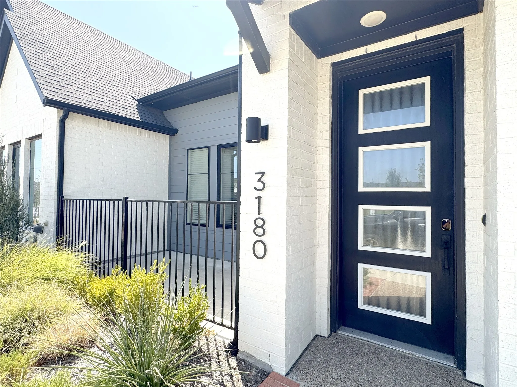 Contemporary exterior with a black framed multi-pane entry door, white brick facade, and dark roofline
