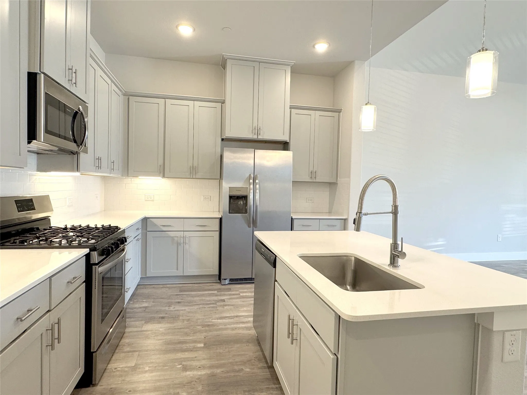 Contemporary kitchen featuring light gray cabinetry, stainless steel appliances, a subway tile backsplash, and an island with an undermount sink and gooseneck faucet