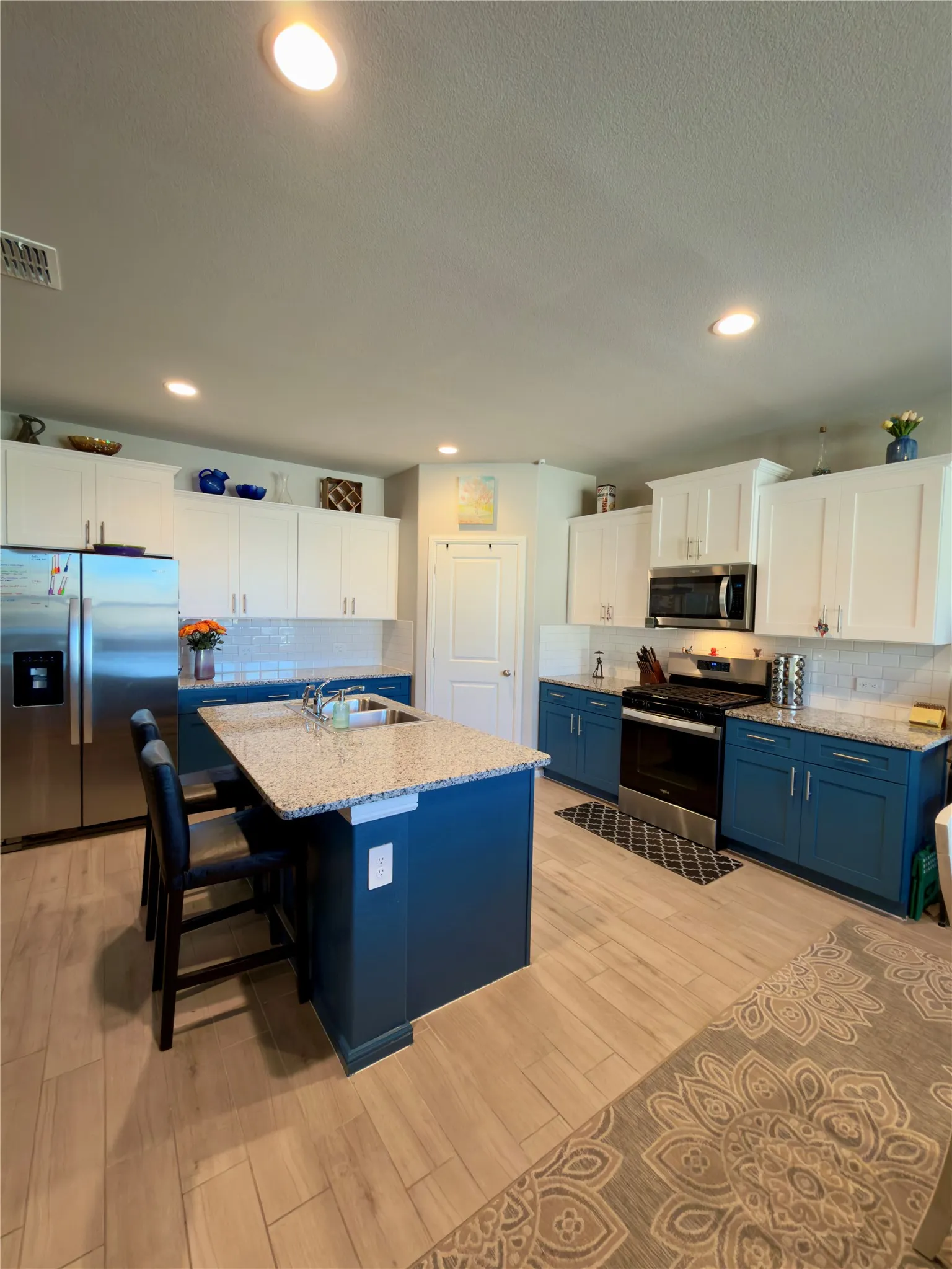 Dual tone kitchen featuring dual tone cabinets, stainless steel appliances, light stone counters, backsplash, and a center island with sink
