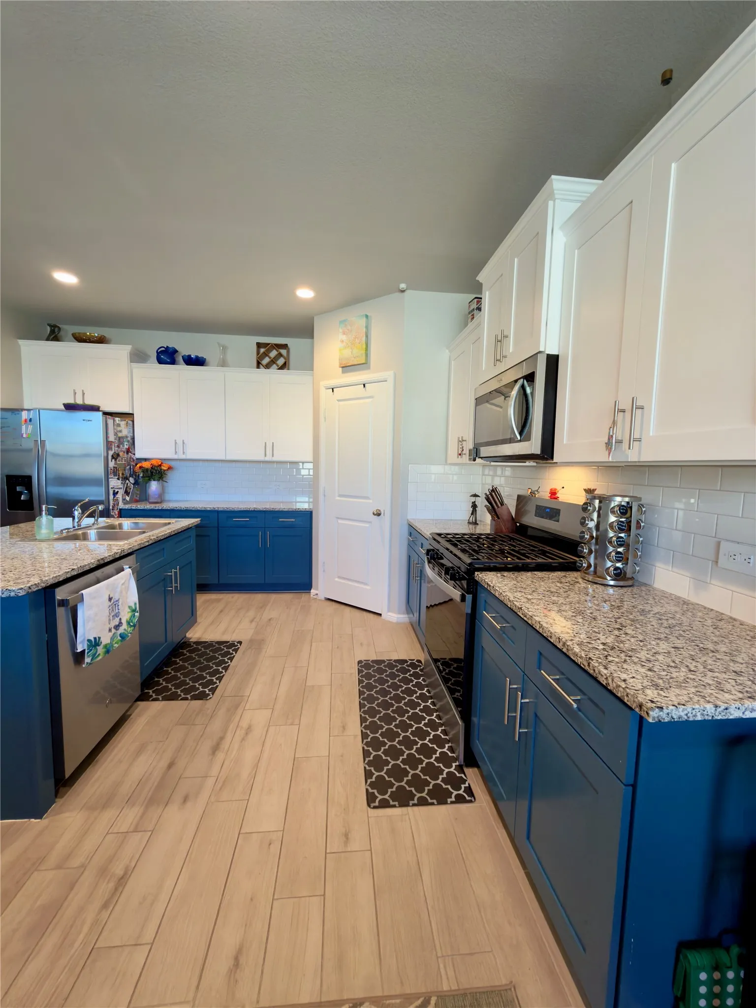Kitchen featuring two tone color scheme, stainless steel appliances, light stone counters, light wood-style flooring, and decorative backsplash