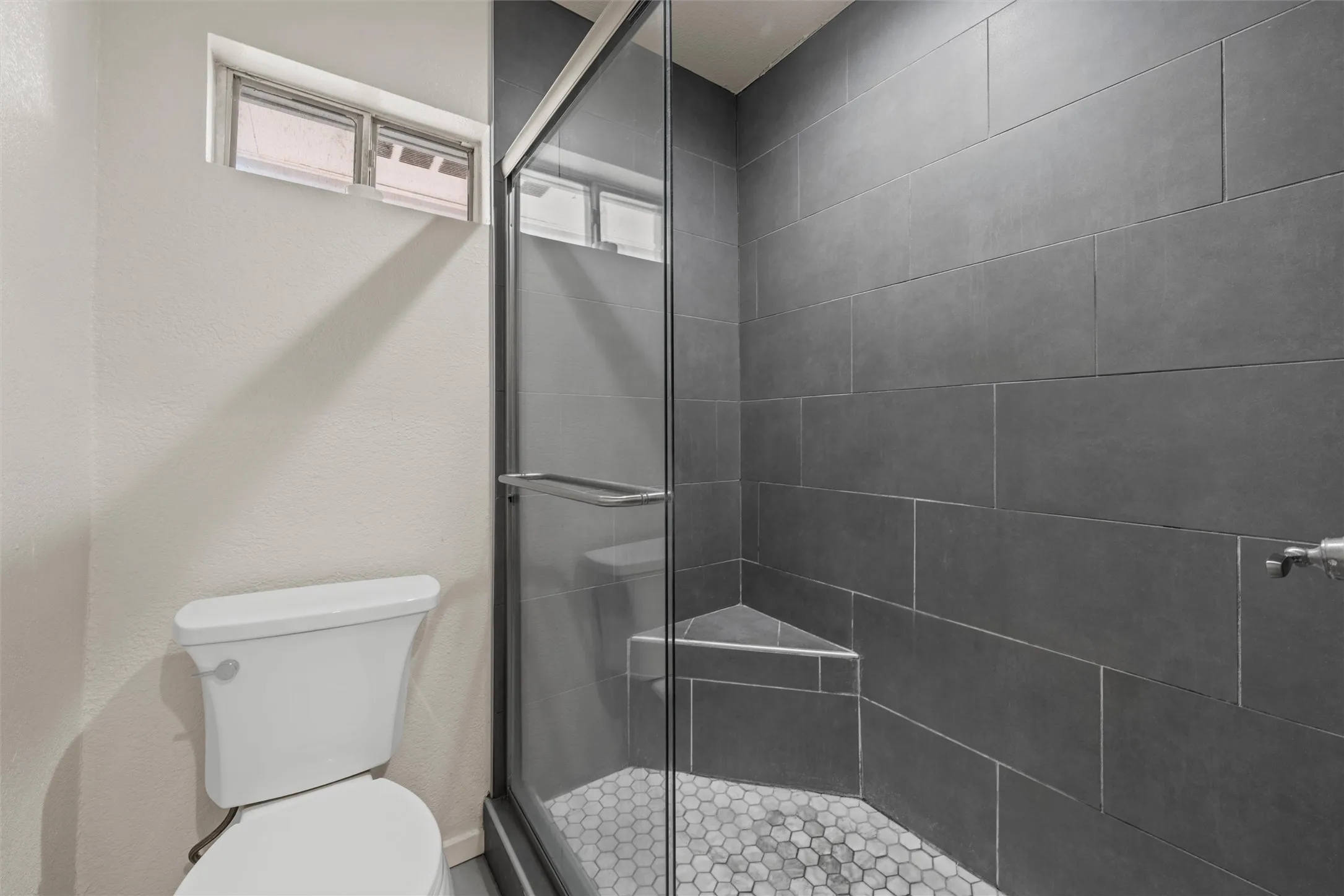 Shower with glass enclosure, dark gray tile walls, and a hexagonal mosaic tile floor