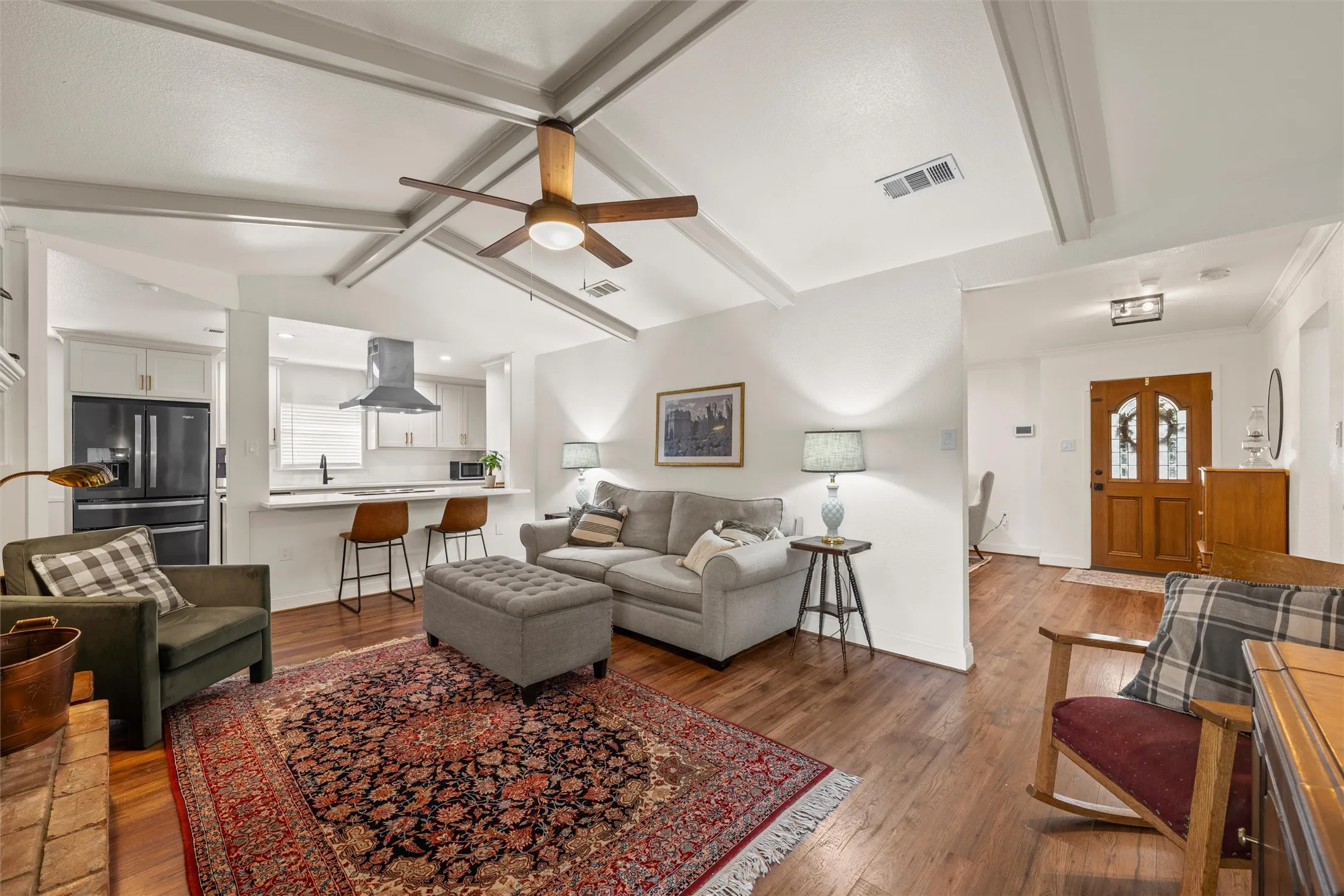 Vaulted ceiling with exposed beams, wood-finish flooring, kitchen with contemporary range hood, breakfast bar, and wood entry door with glass inserts