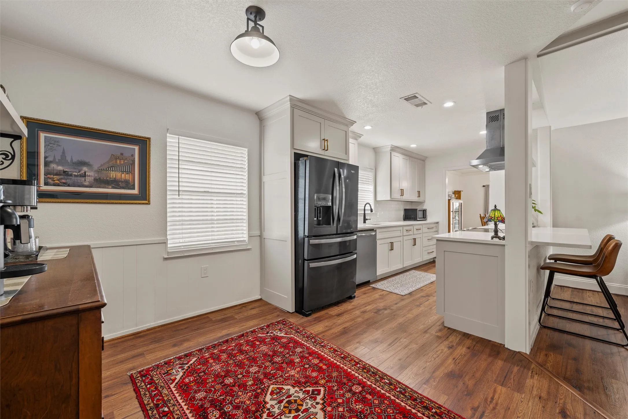 Wood-finish flooring, white cabinetry, integrated black appliances, pendant lighting, and a breakfast bar