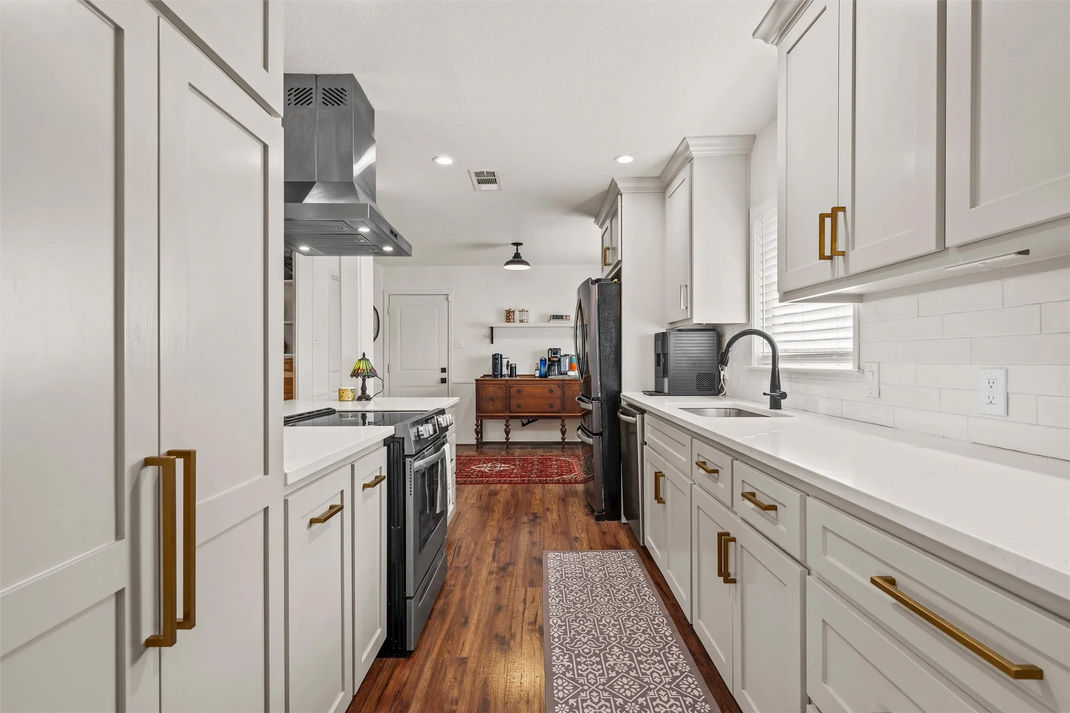 Galley kitchen featuring white shaker cabinetry, white countertops, stainless steel appliances, wood-finish flooring, and subway tile backsplash