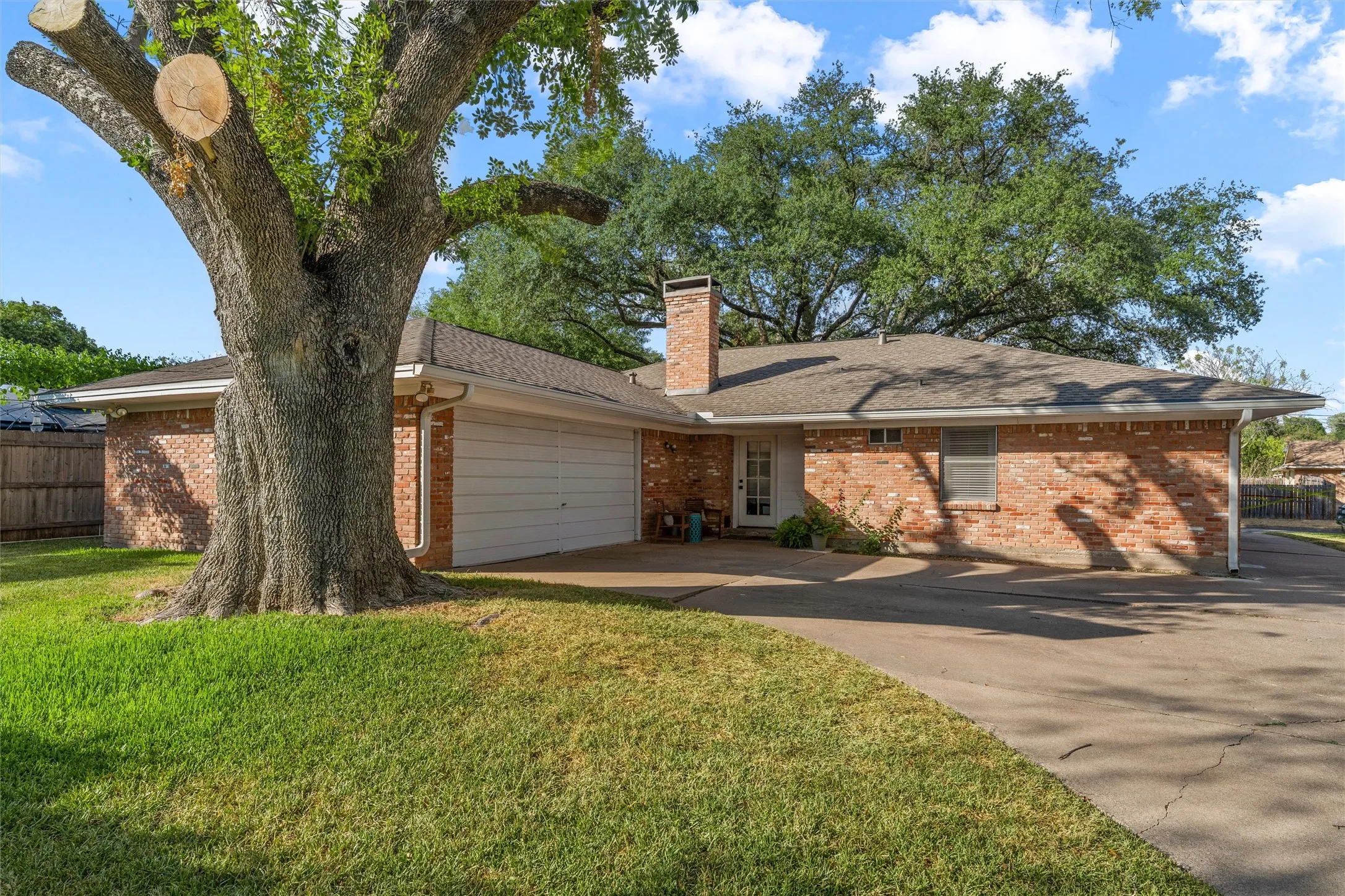 Brick exterior, attached garage, composition shingle roof, mature tree, and concrete driveway