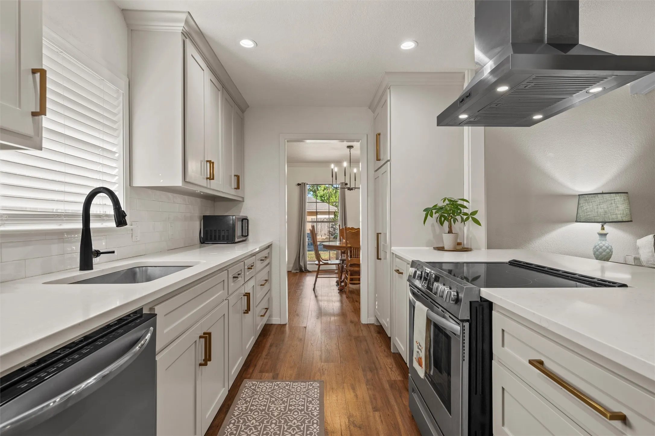 Galley kitchen featuring white cabinetry, light countertops, wood-finish flooring, a stainless steel range hood, and a black faucet