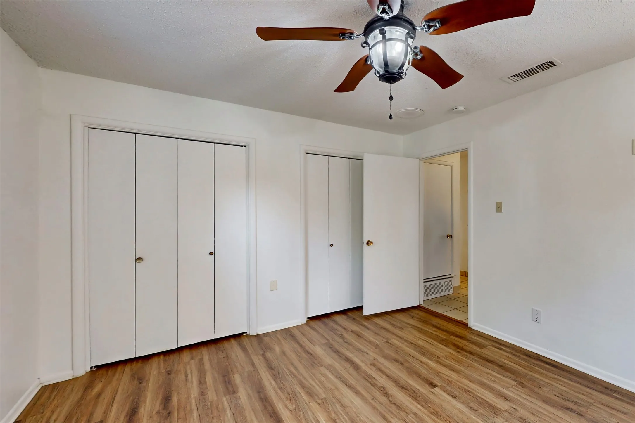 Primary bedroom has a connected dual-closet, ceiling fans and wood-look luxury vinyl plank flooring.