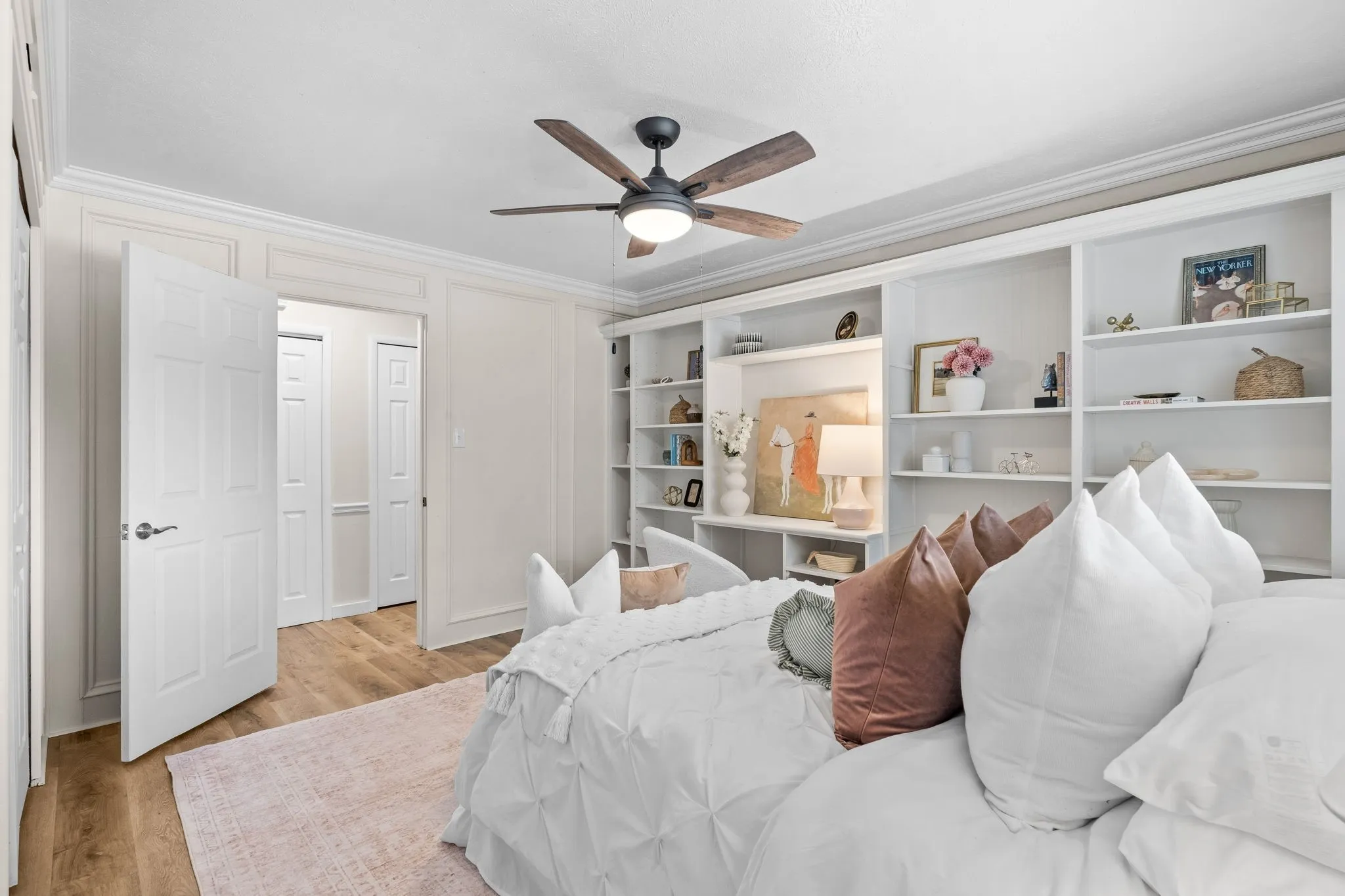 Built-in shelving, wood-finish flooring, ceiling fan, crown molding, and paneled walls