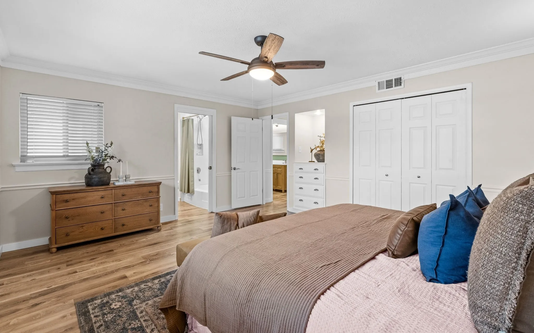 Wood-finish flooring, crown molding, ceiling fan, bi-fold closet doors, and window with blinds