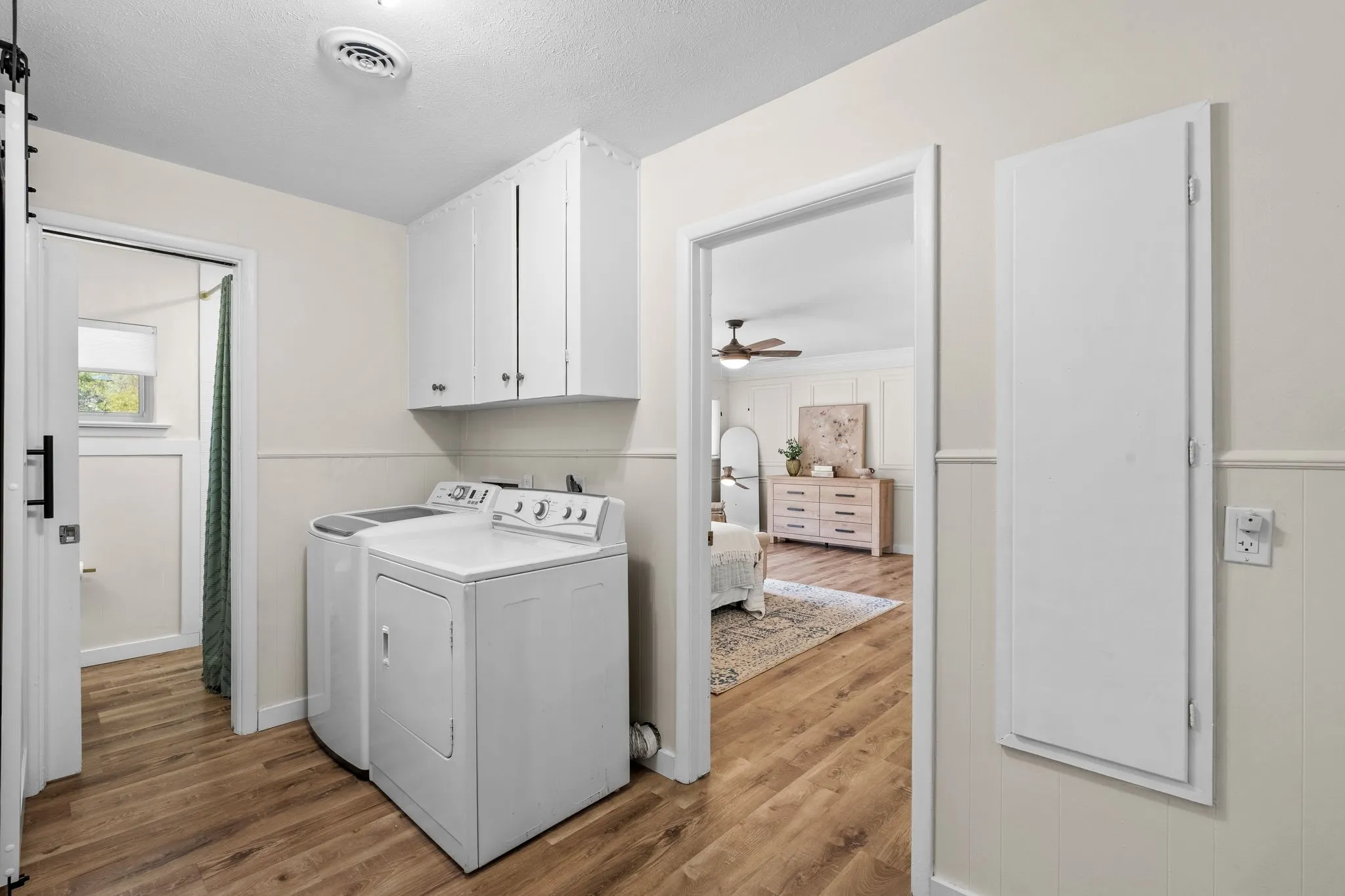 Laundry area featuring white cabinetry, wood-finish flooring, and wainscoting