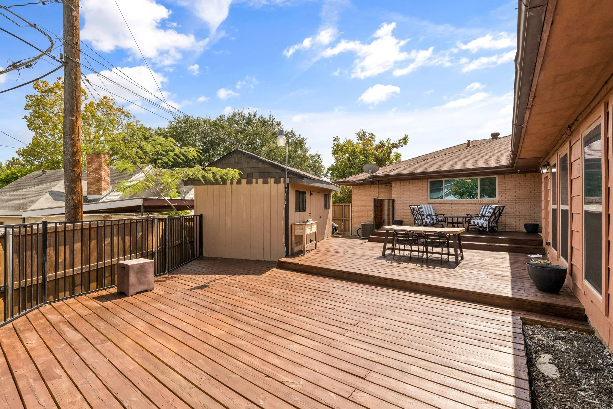 Expansive multi-level wood deck with a privacy fence, featuring a brick exterior and a separate storage structure