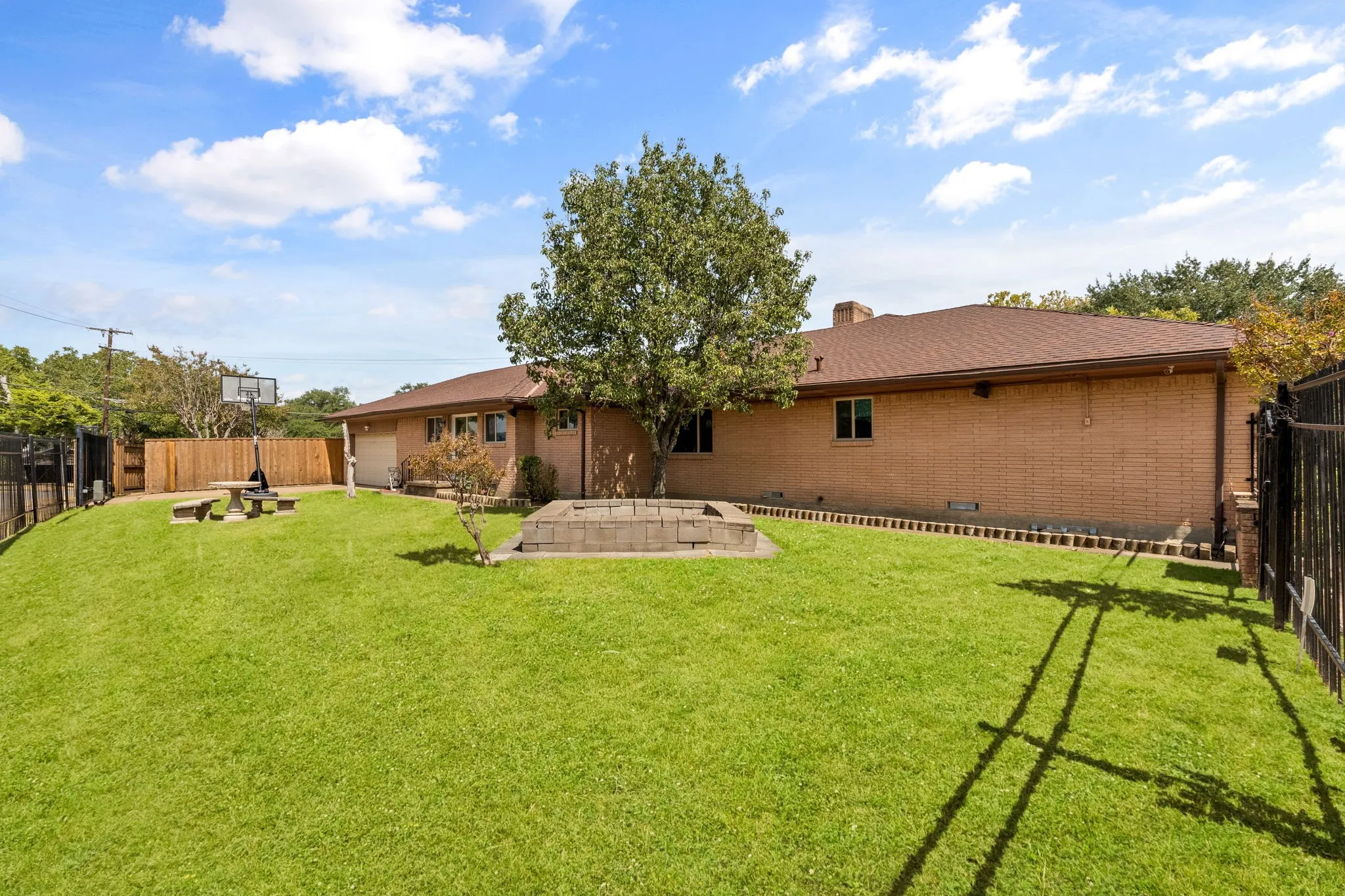 Expansive rear yard featuring green lawn, a mature shade tree, brick exterior, and a privacy fence