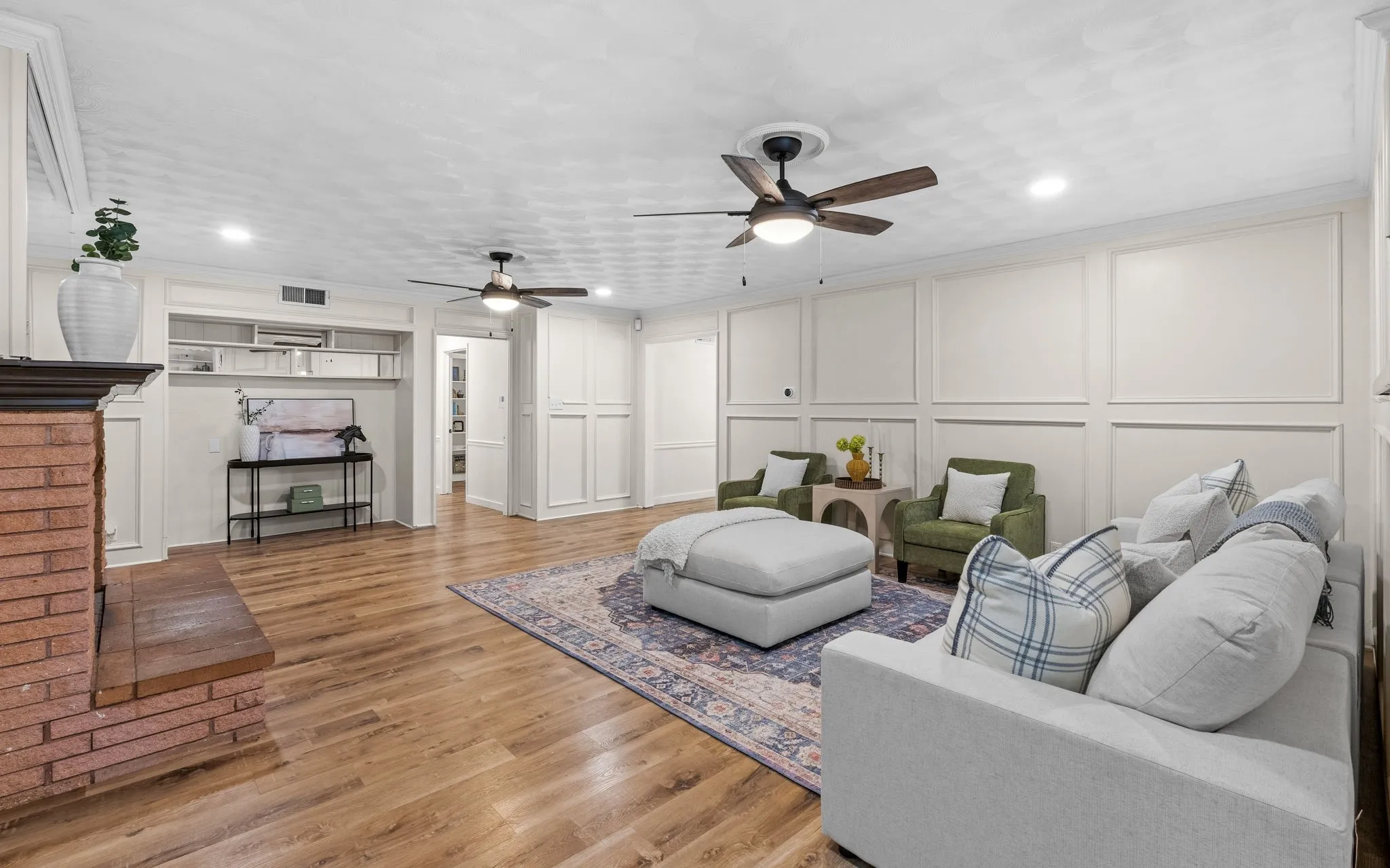 Wood-finish flooring throughout, brick fireplace with a wood mantle, recessed lighting, and dual ceiling fans