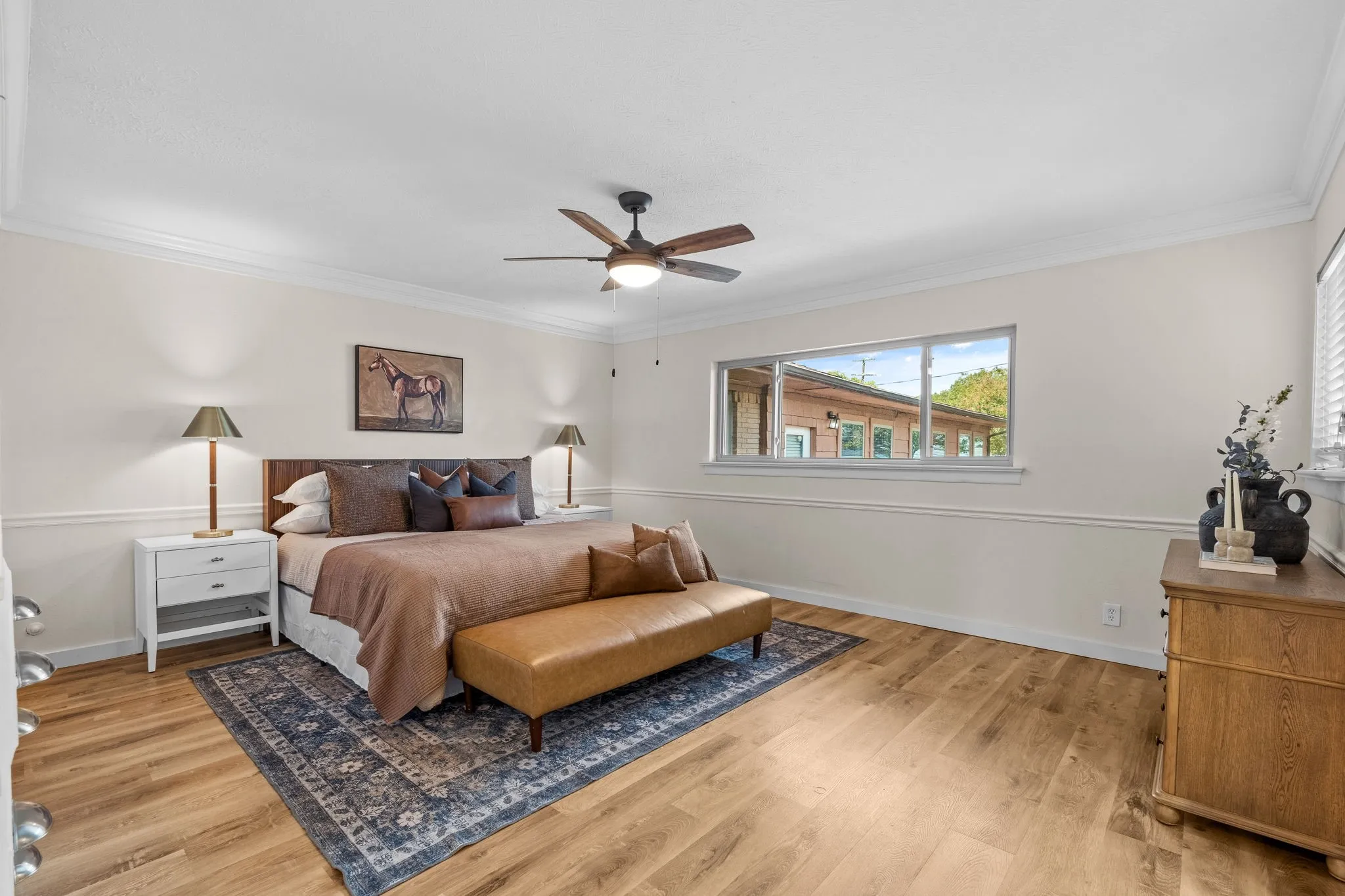 Wood-finish flooring, crown molding, a ceiling fan with integrated lighting, and a large window