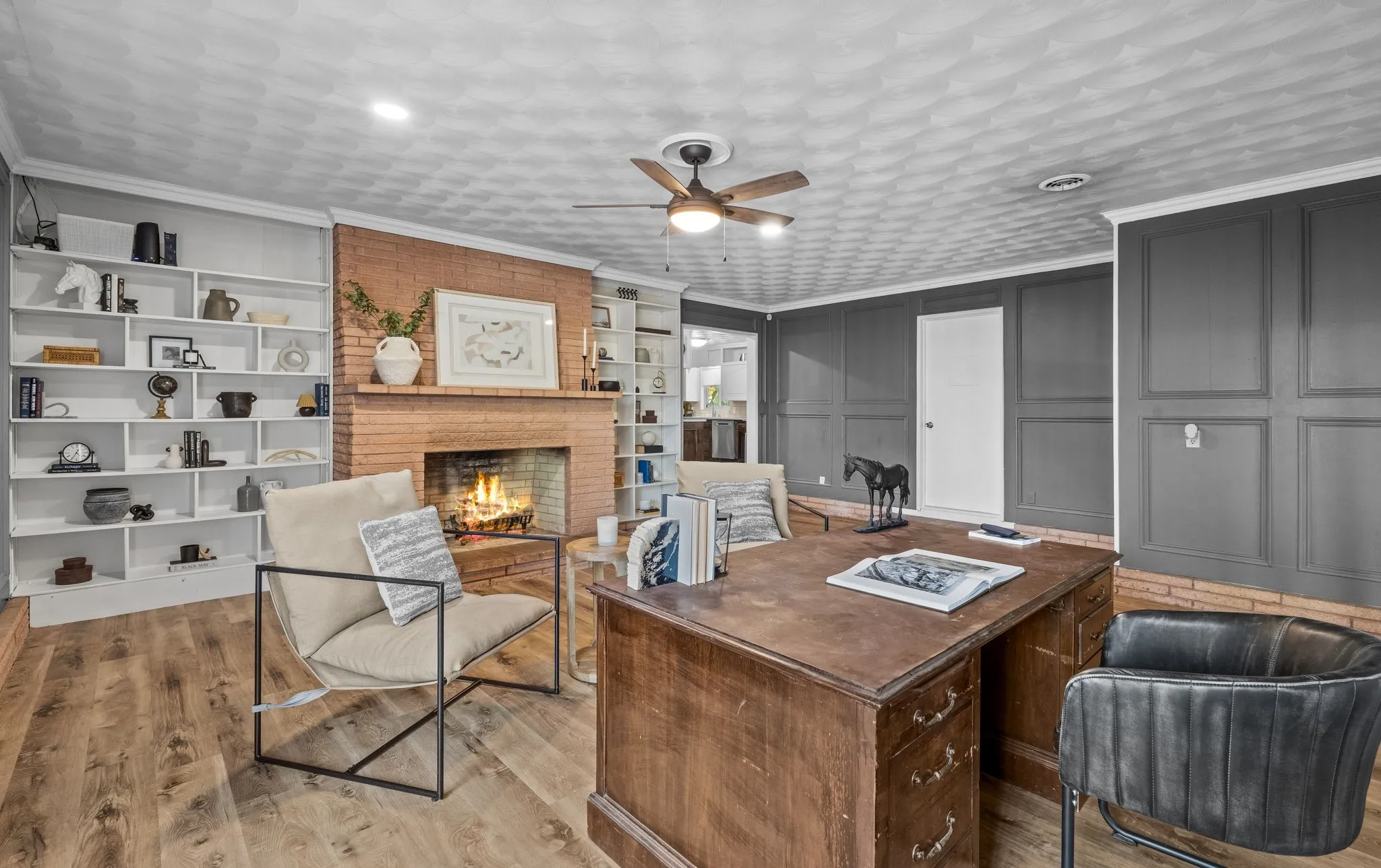 Brick fireplace with a substantial hearth, built-in shelving, wood-finish flooring, and crown molding