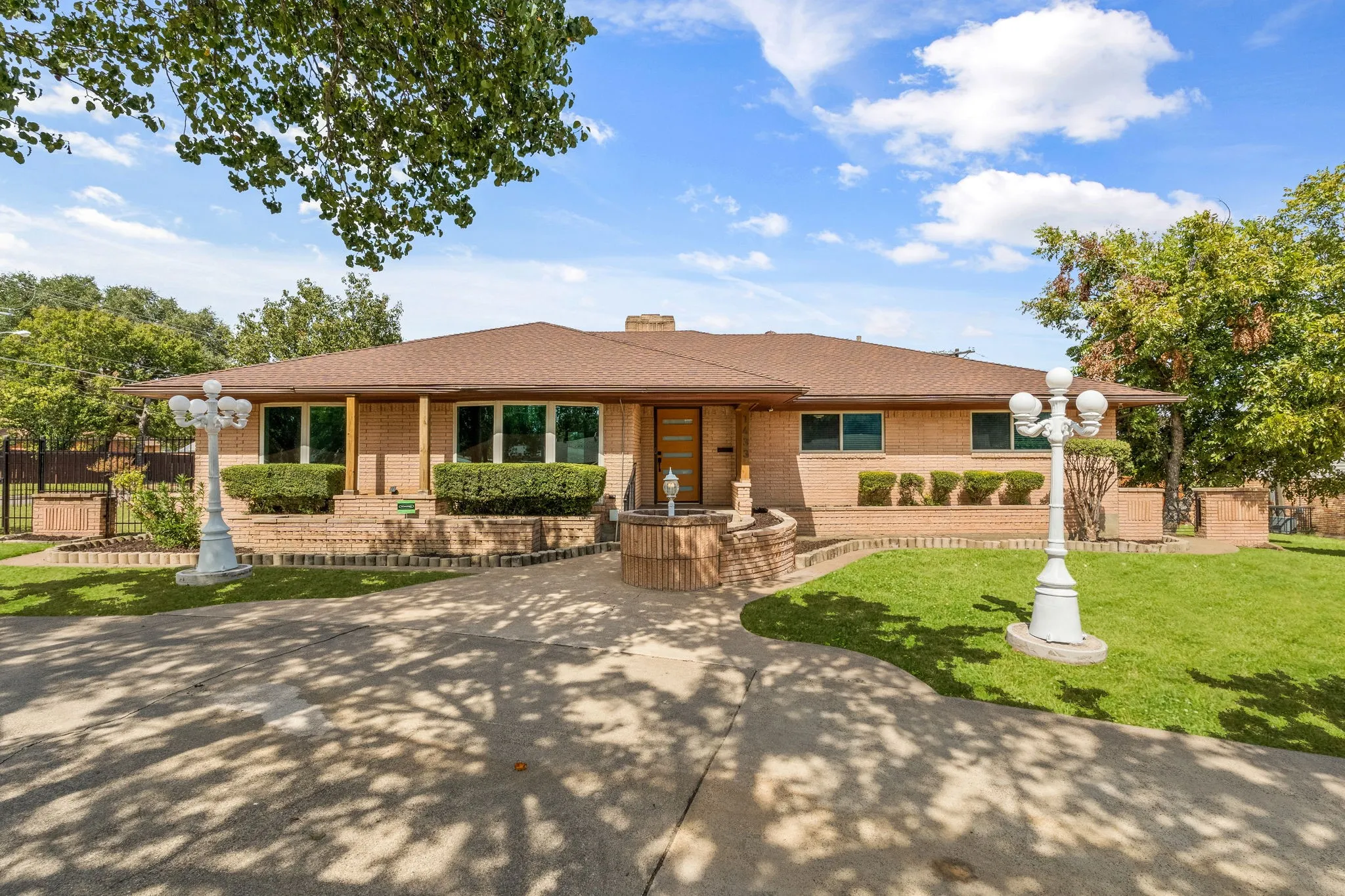 Brick exterior with a brown shingle roof, a paved circular driveway, and a front porch with wood columns
