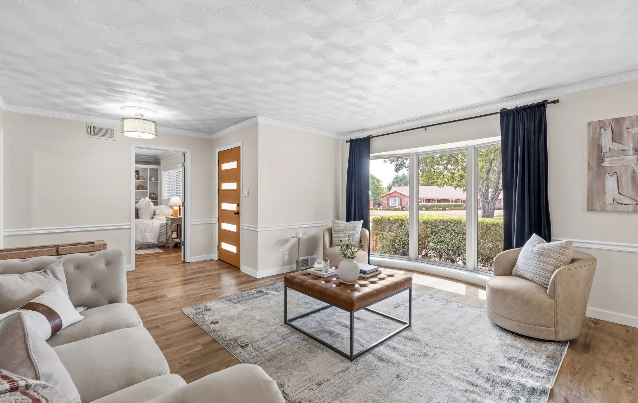 Wood-finish flooring throughout, bay window with exterior landscaping, decorative ceiling texture, modern light fixture, and a light wood-tone interior door