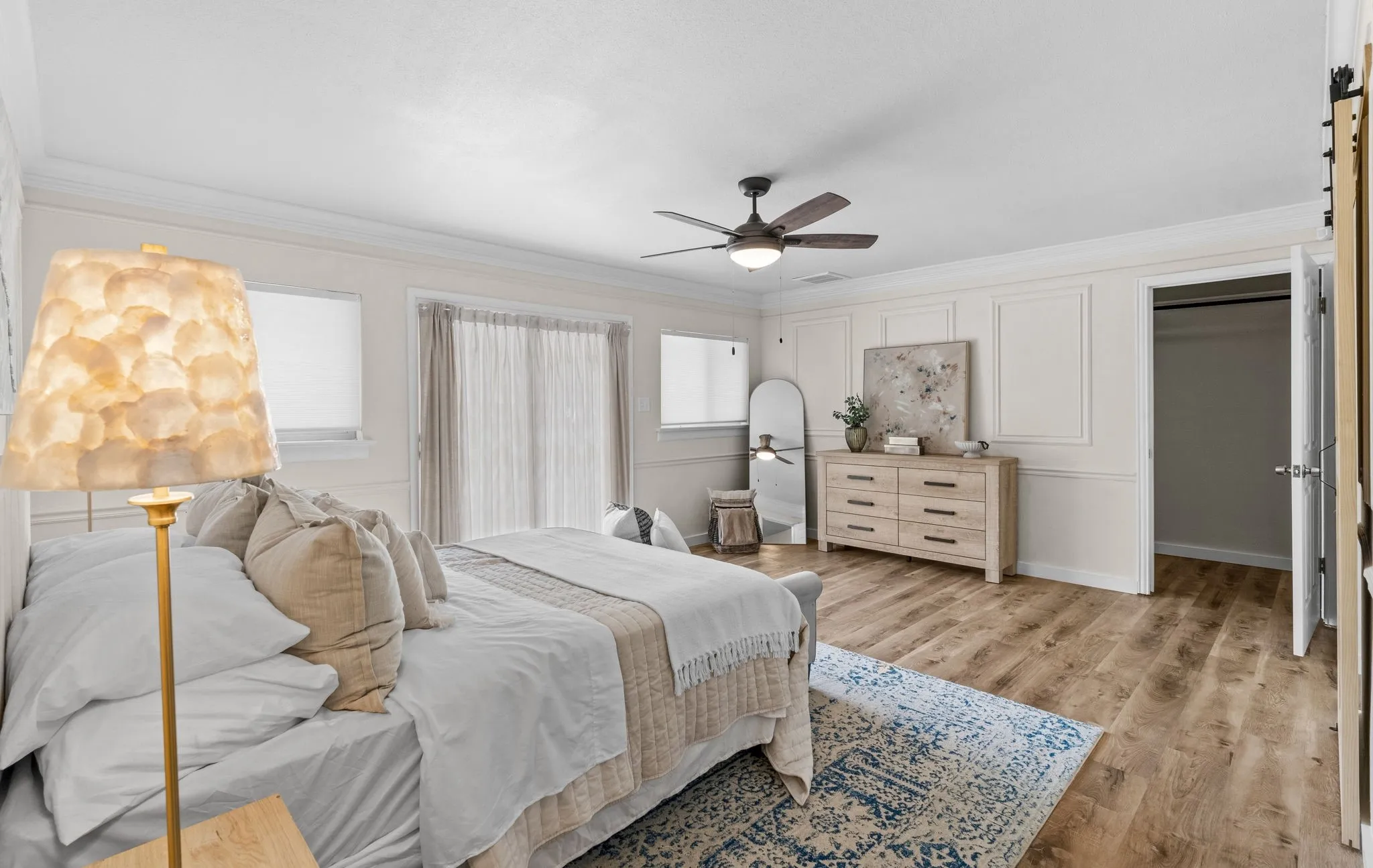 Wood-finish flooring throughout, ceiling fan with integrated lighting, paneled wall detailing, sliding glass door, and a built-in closet