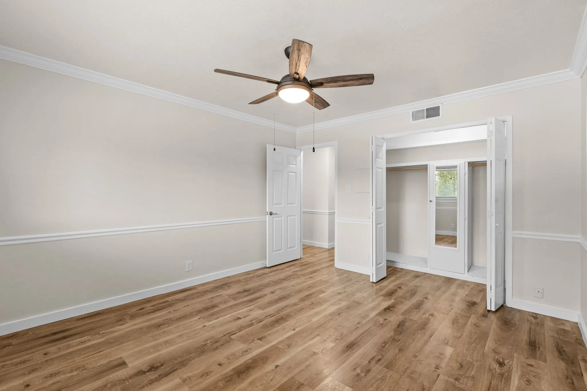 Wood-finish flooring, crown molding, chair rail molding, ceiling fan with integrated lighting, and bi-fold closet doors