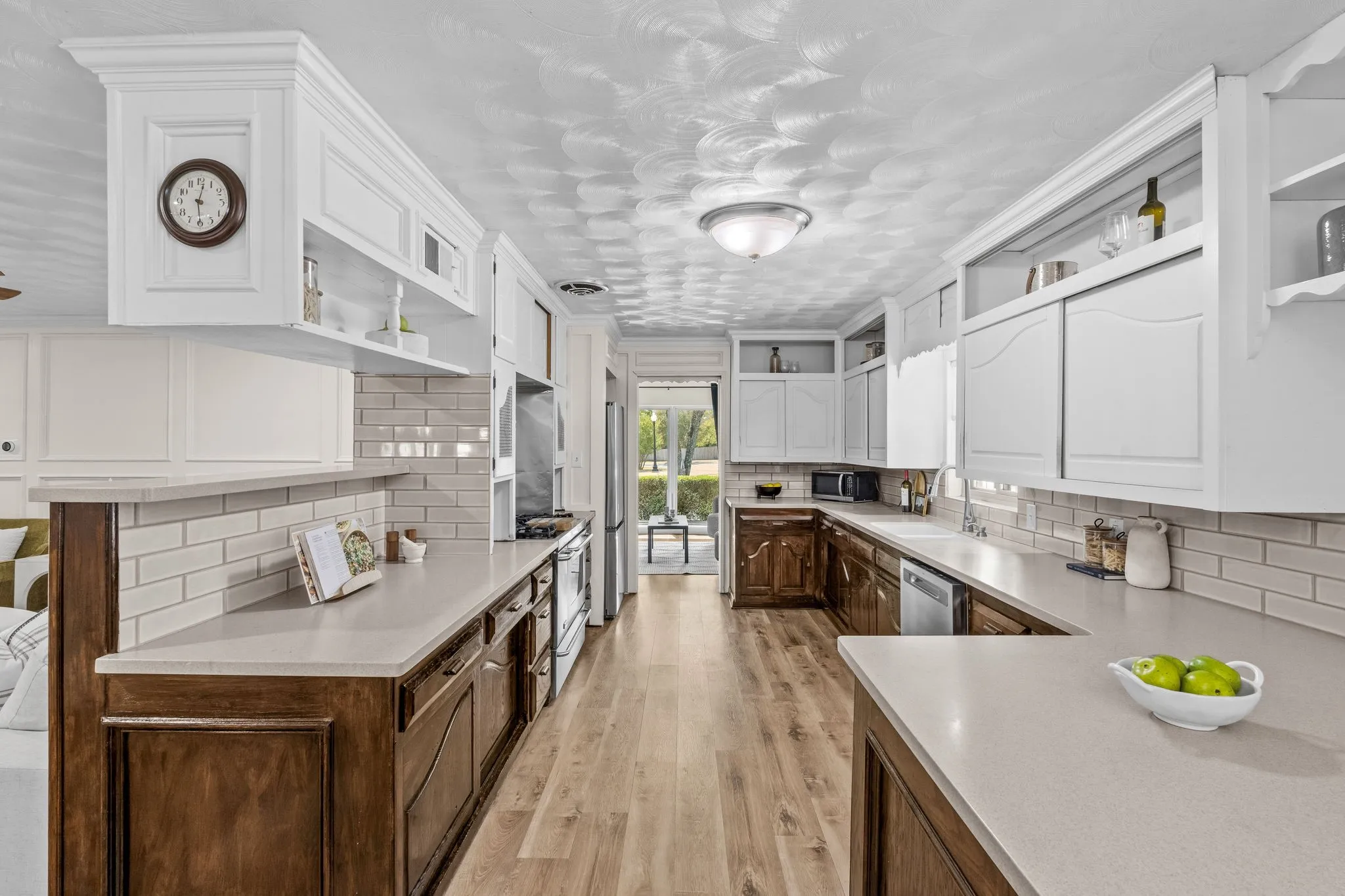 Kitchen featuring light wood-finish flooring, white subway tile backsplash, light countertops, wood-finish lower cabinetry, and white upper cabinetry